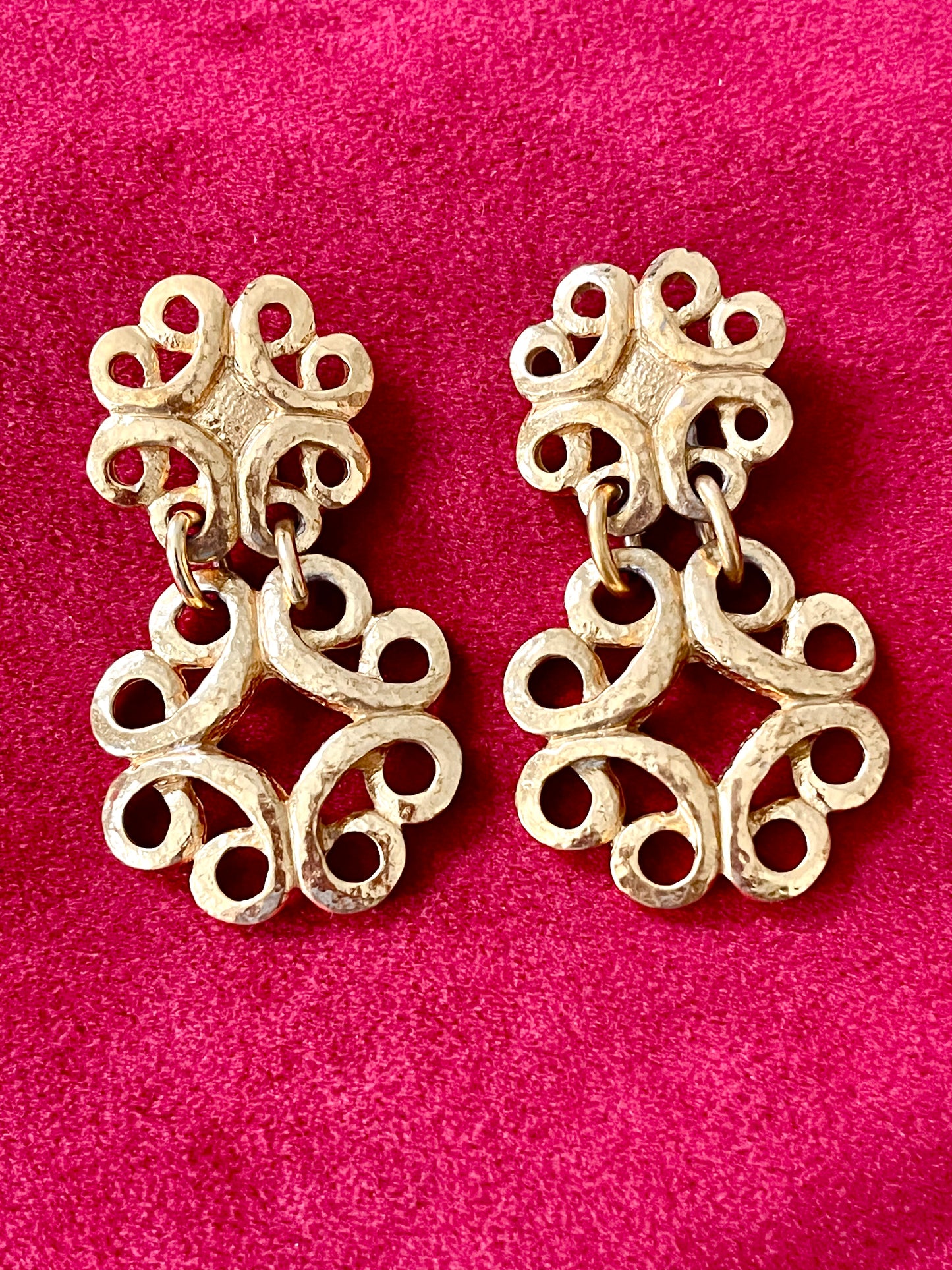 Front view of vintage gold-tone Yves Saint Laurent statement drop earrings displayed on a red background,