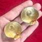 Back side view Gold-tone 80s vintage Yves Saint Laurent shell-shaped earrings displayed on hand and a red fabric showing detailed signature and hallmark 