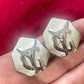 Close-up of vintage YSL silver-tone hexagon earrings resting on the hand, showing the textured surface and raised YSL monogram.