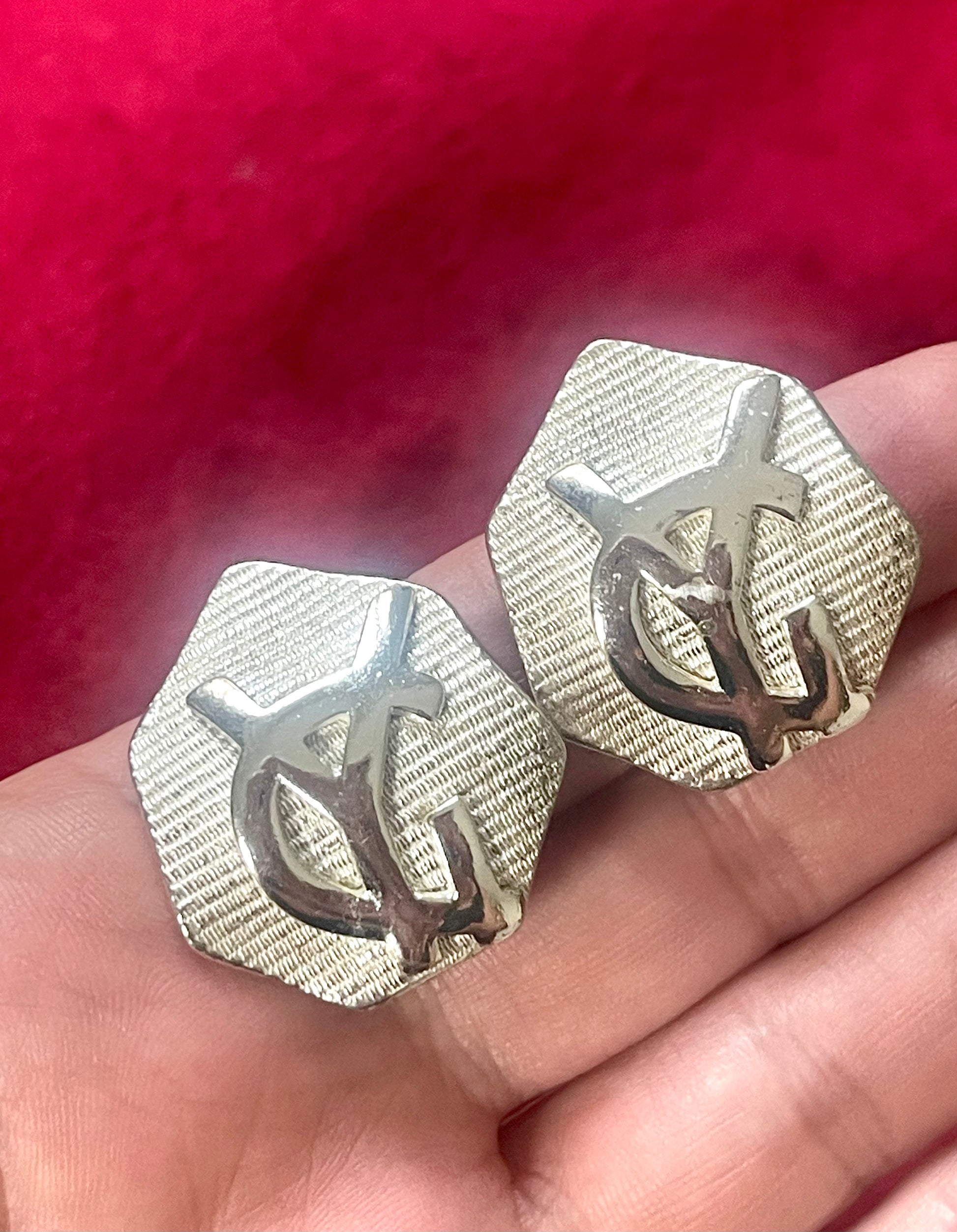 Close-up of vintage YSL silver-tone hexagon earrings resting on the hand, showing the textured surface and raised YSL monogram.