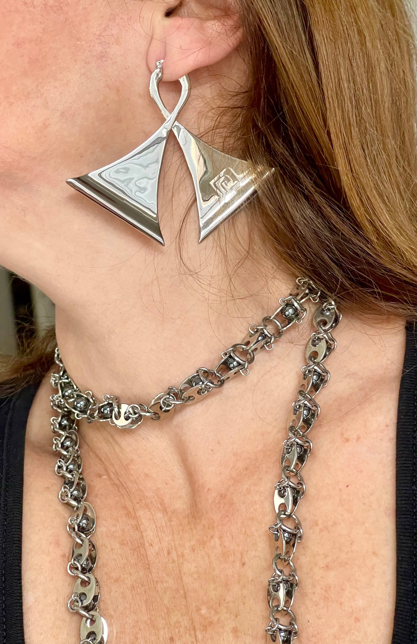 Close-up of a person wearing vintage Paco Rabanne geometric silver earrings and a chain necklace.