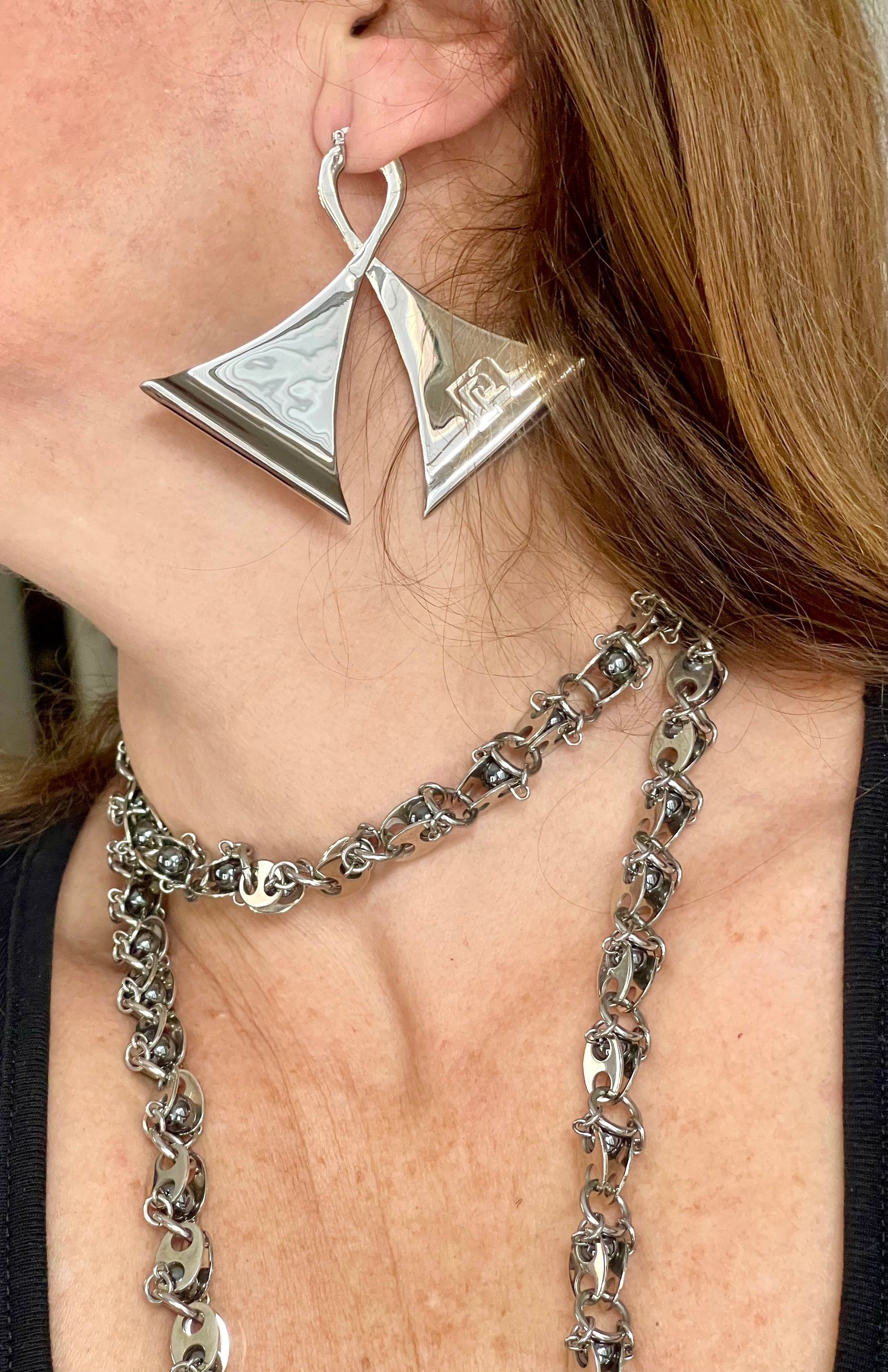 Close-up of a person wearing vintage Paco Rabanne geometric silver earrings and a chain necklace.