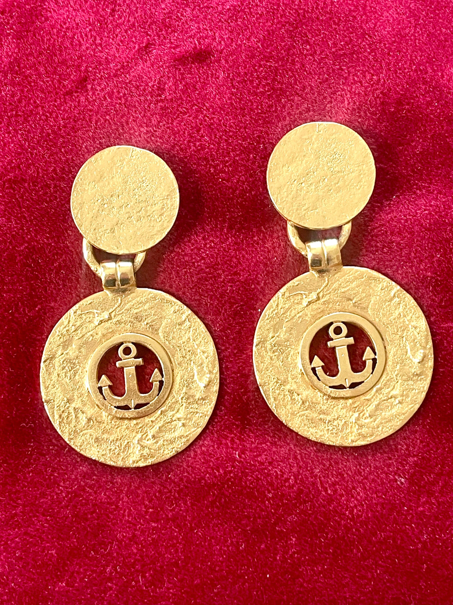 Vintage 1980s Yves Saint Laurent gold-tone anchor earrings with textured circular drop, clip-on design on red background 