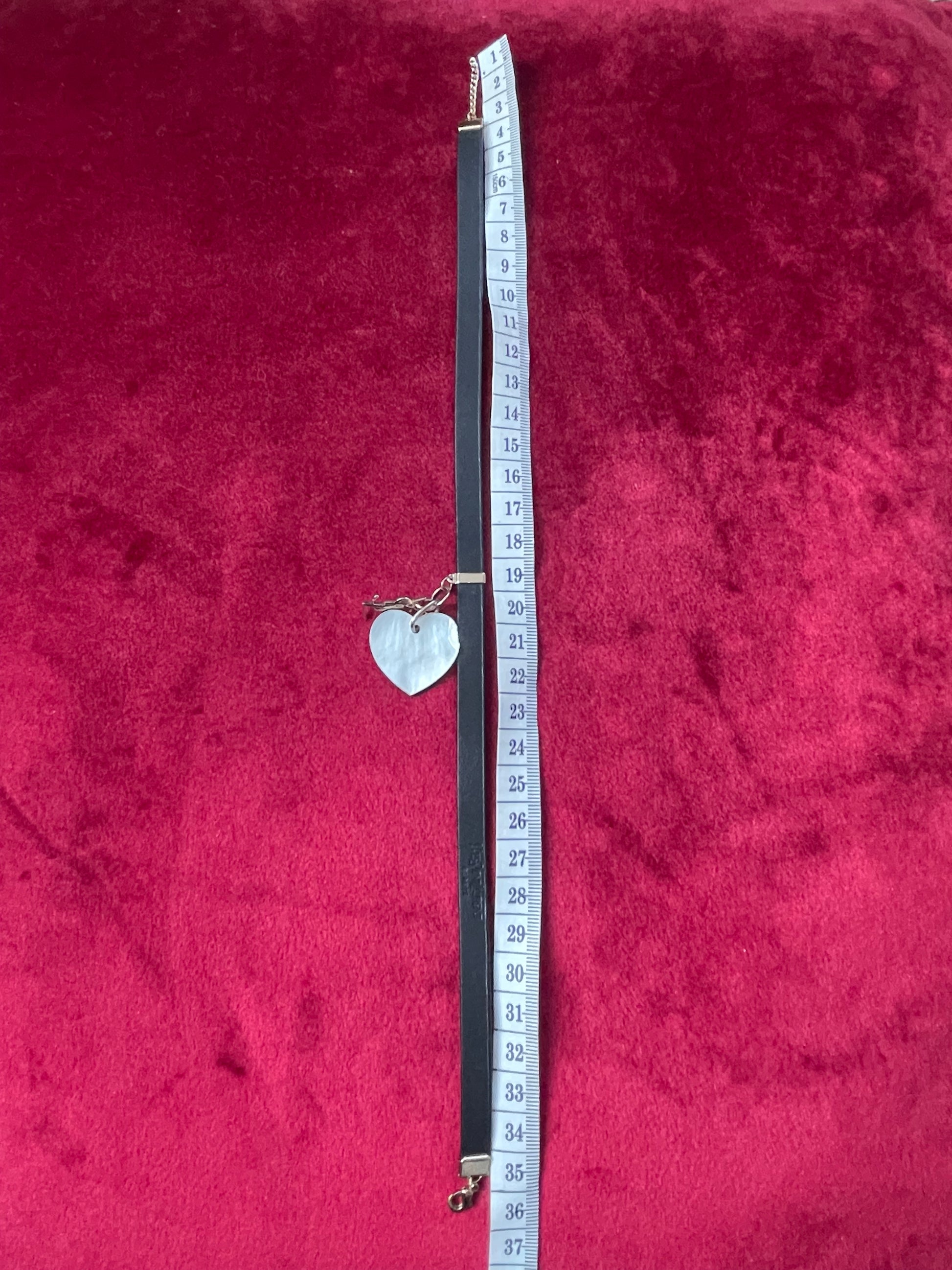 Tape measured on a red textured fabric background of a vintage Yves Saint Laurent heart seashell pendant YSL charm mounted on a black leather YSL Parfums necklace.