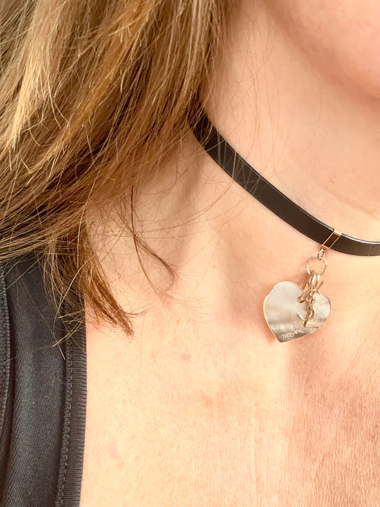 Side view of Person wearing a black leather Yves Saint Laurent choker necklace with a heart-shaped pendant and logo charm YSL
