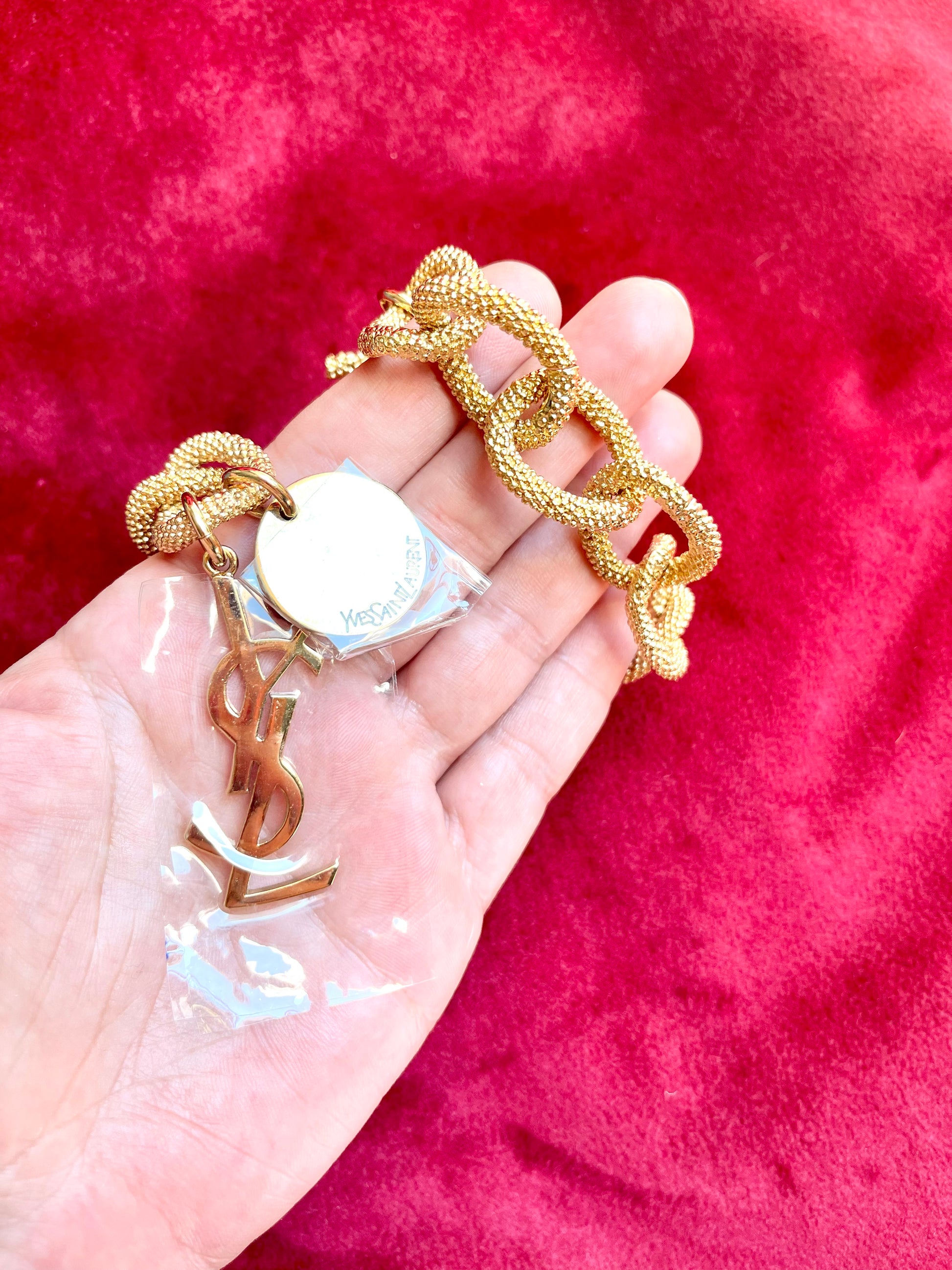 Displayed on hand Detail view of YSL monogram charm hanging from gold vintage Yves Saint Laurent bracelet.
