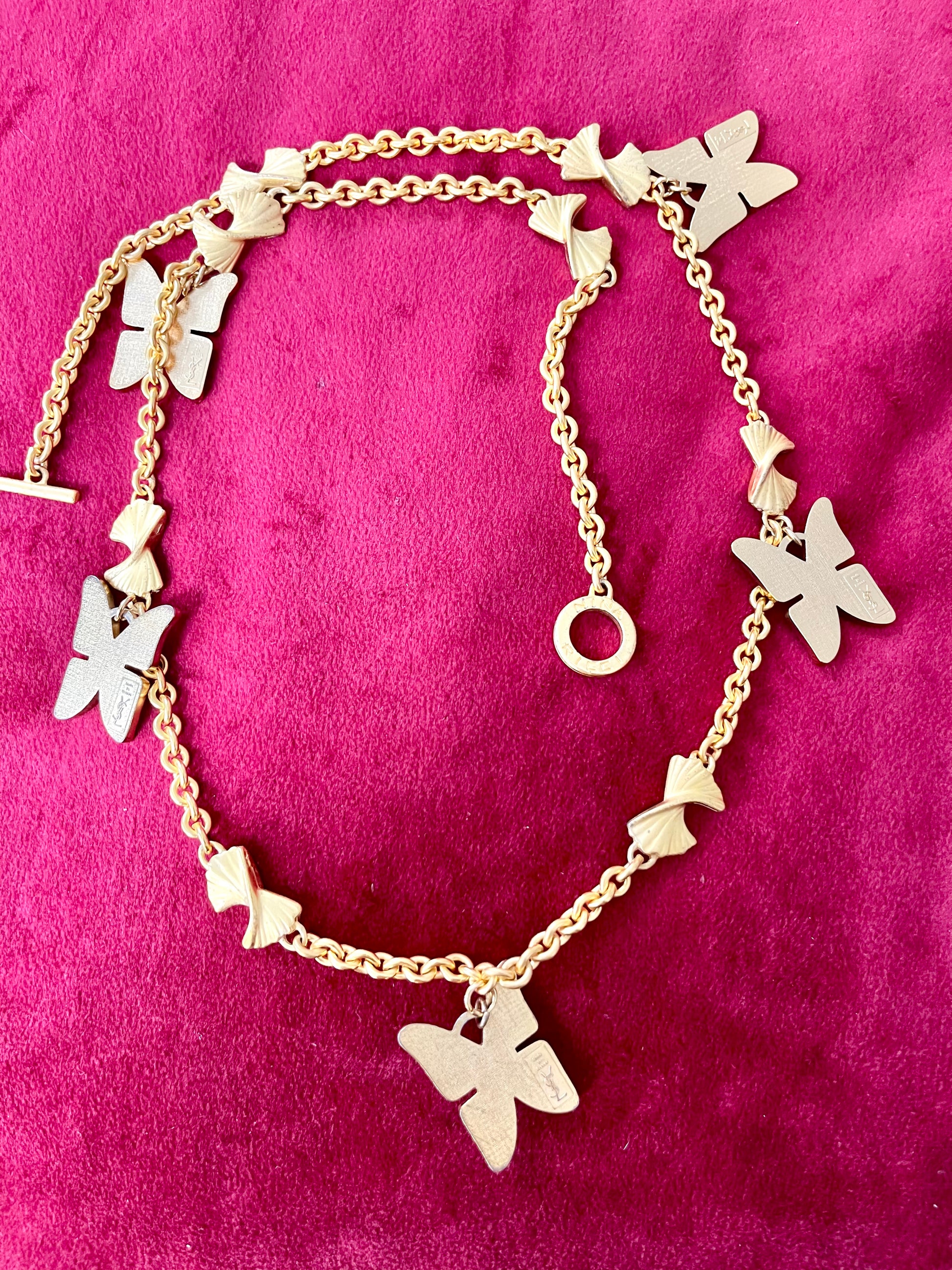 Back side view of Vintage 80s five Yves Saint Laurent Butterfly Enameled pendants mounted on a Nina Ricci gold necklace, displayed on a red velvet background 