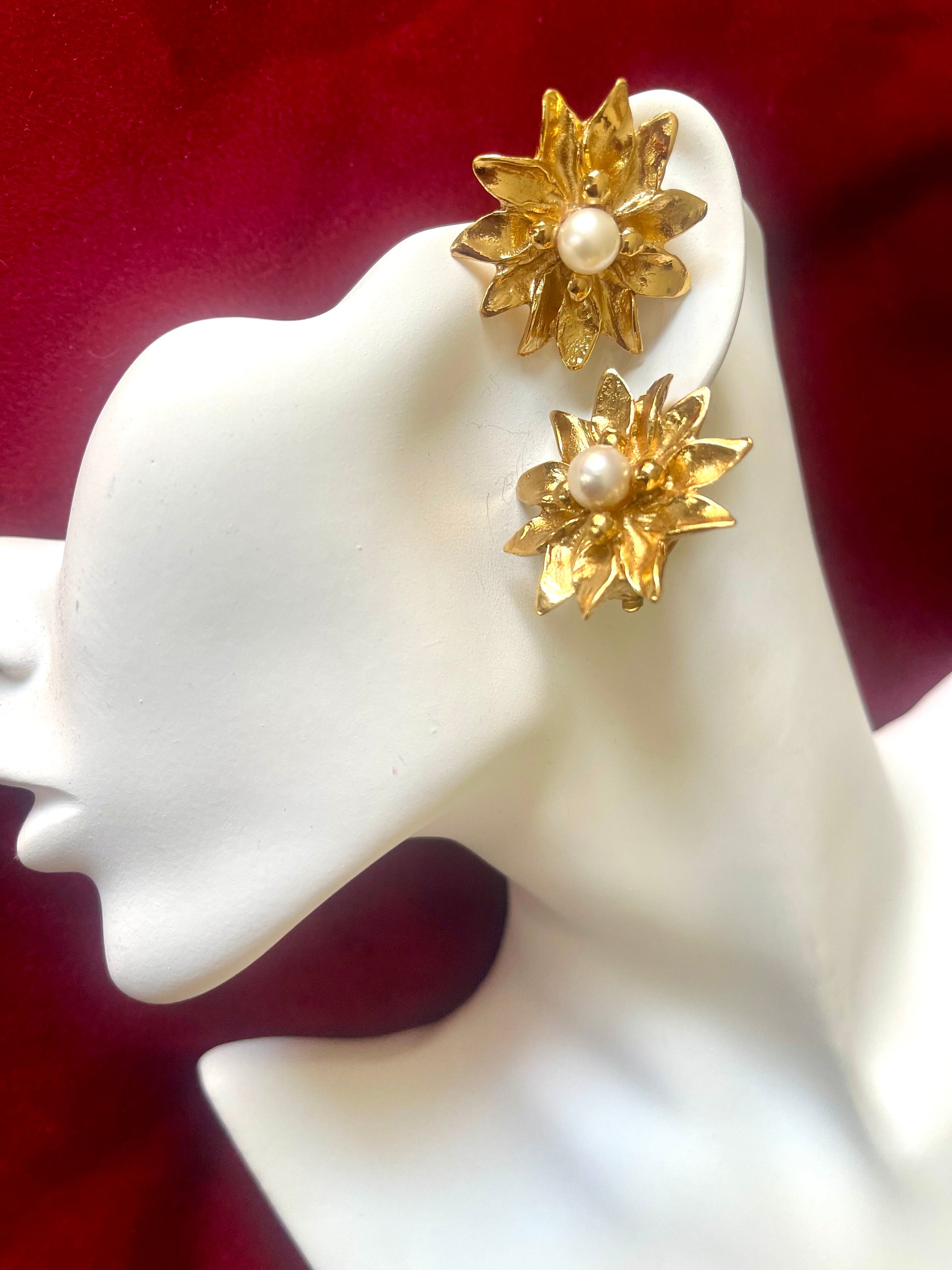 Gold floral vintage Yves Saint Laurent earrings with pearl centers on a white mannequin head against a red background
