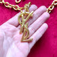Displayed on hand Authentic YSL oversized gold logo bag charm pendant repurposed into a long chain necklace, close-up detail vintage Yves Saint Laurent 