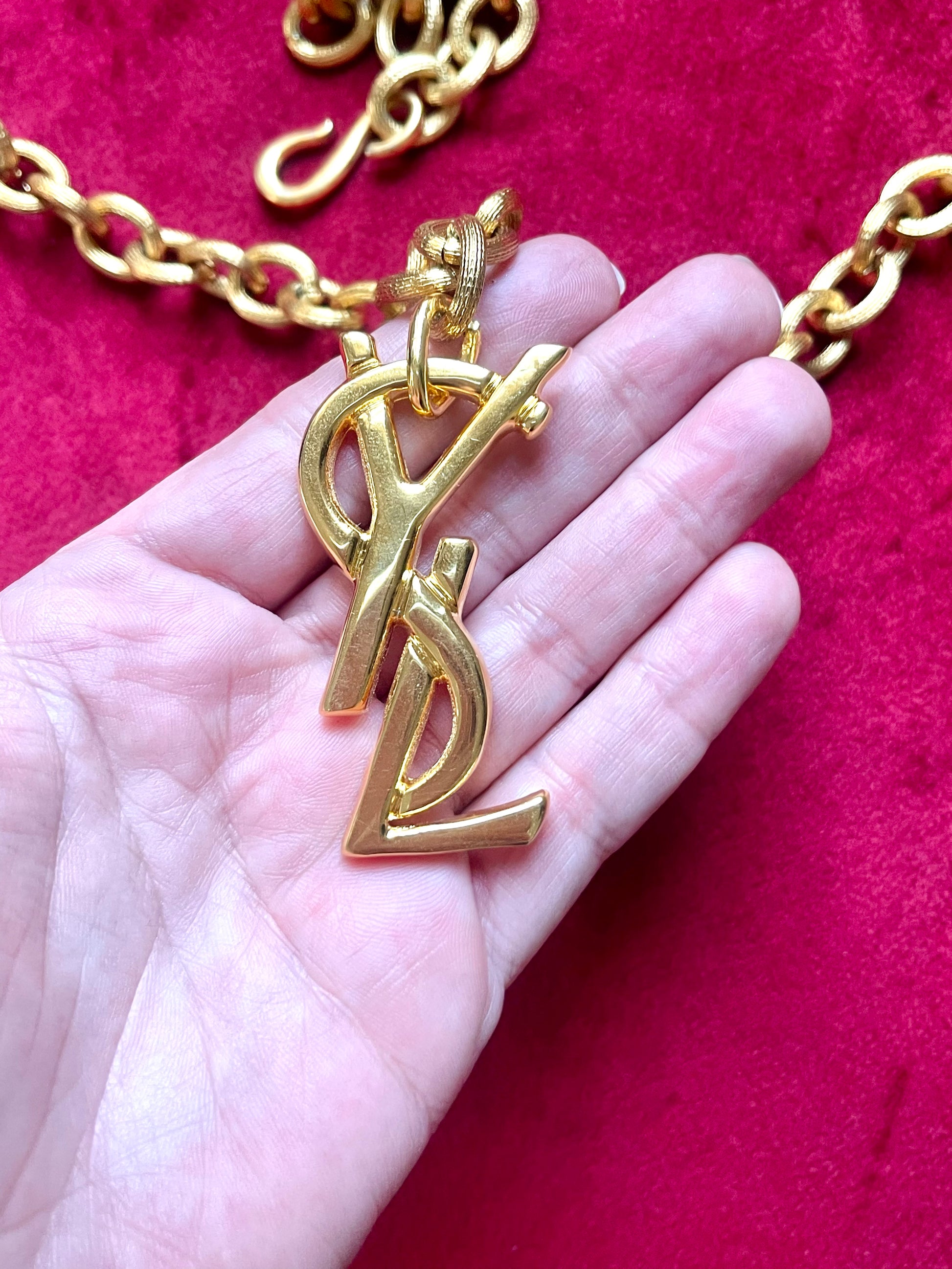 Displayed on hand Authentic YSL oversized gold logo bag charm pendant repurposed into a long chain necklace, close-up detail vintage Yves Saint Laurent 