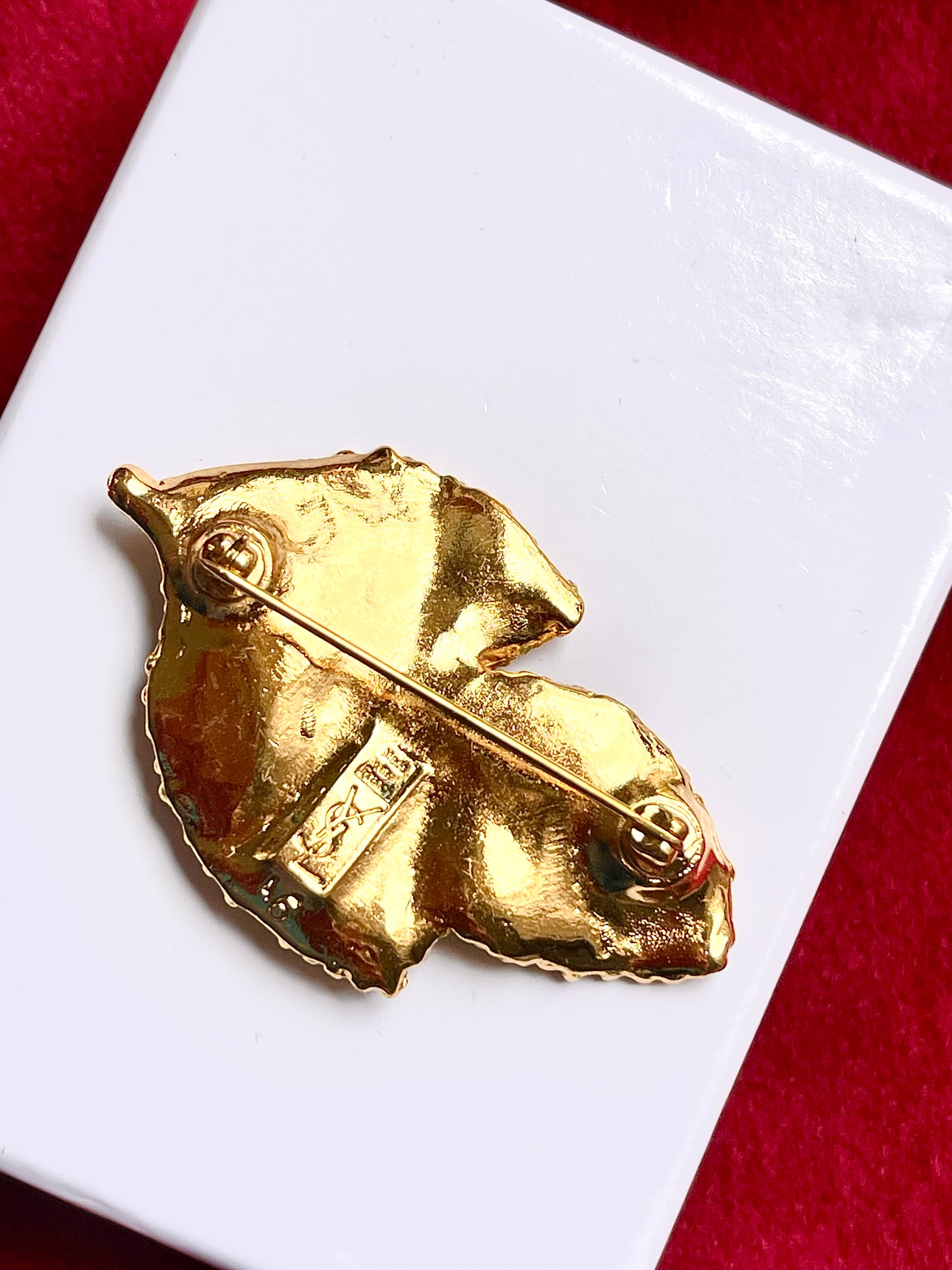 Back view Vintage Yves Saint Laurent 80s 90s gold tone leaf brooch excellent condition on white and red background 