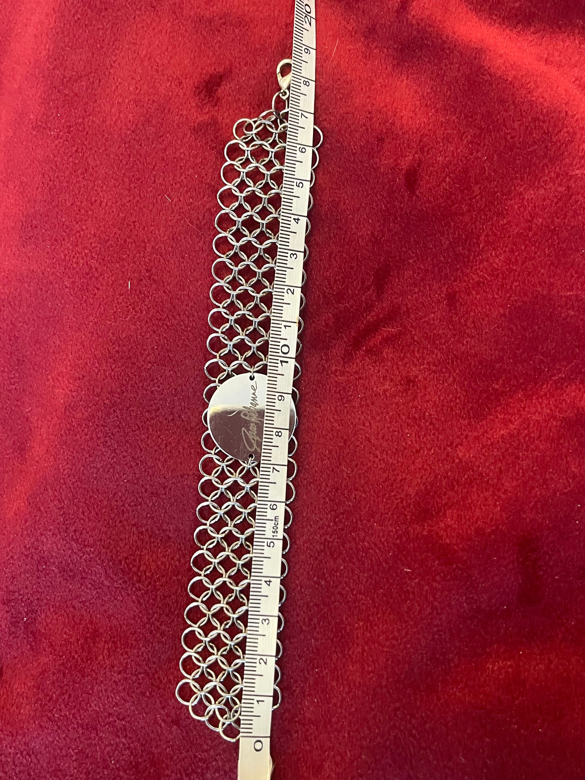 Silver chainmaille Paco Rabanne bracelet with a ruler for scale on a red background
