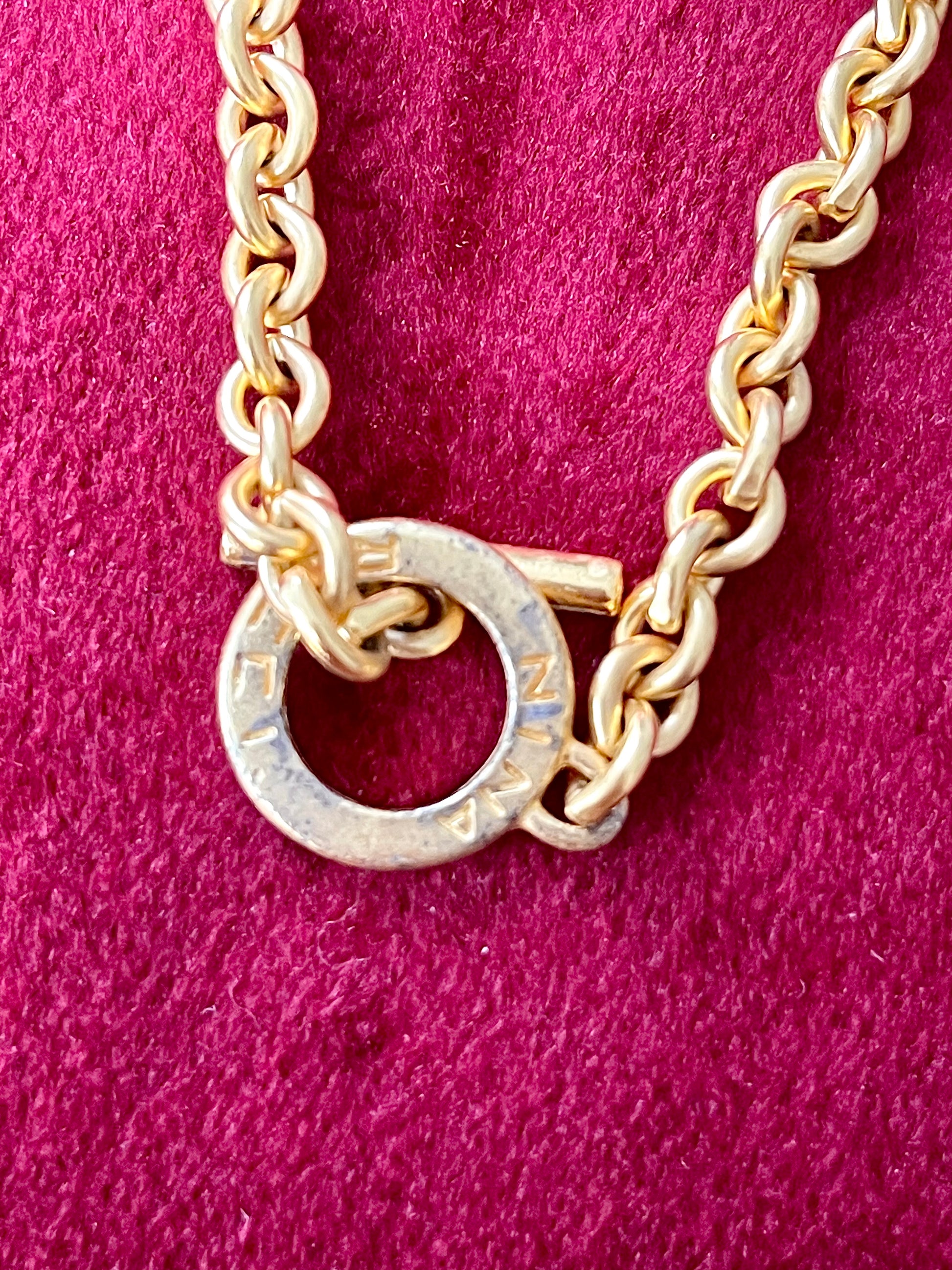 Detailed view of oxidation and patina on vintage Nina Ricci chain holding multiple YSL pendants on red velvet fabric.