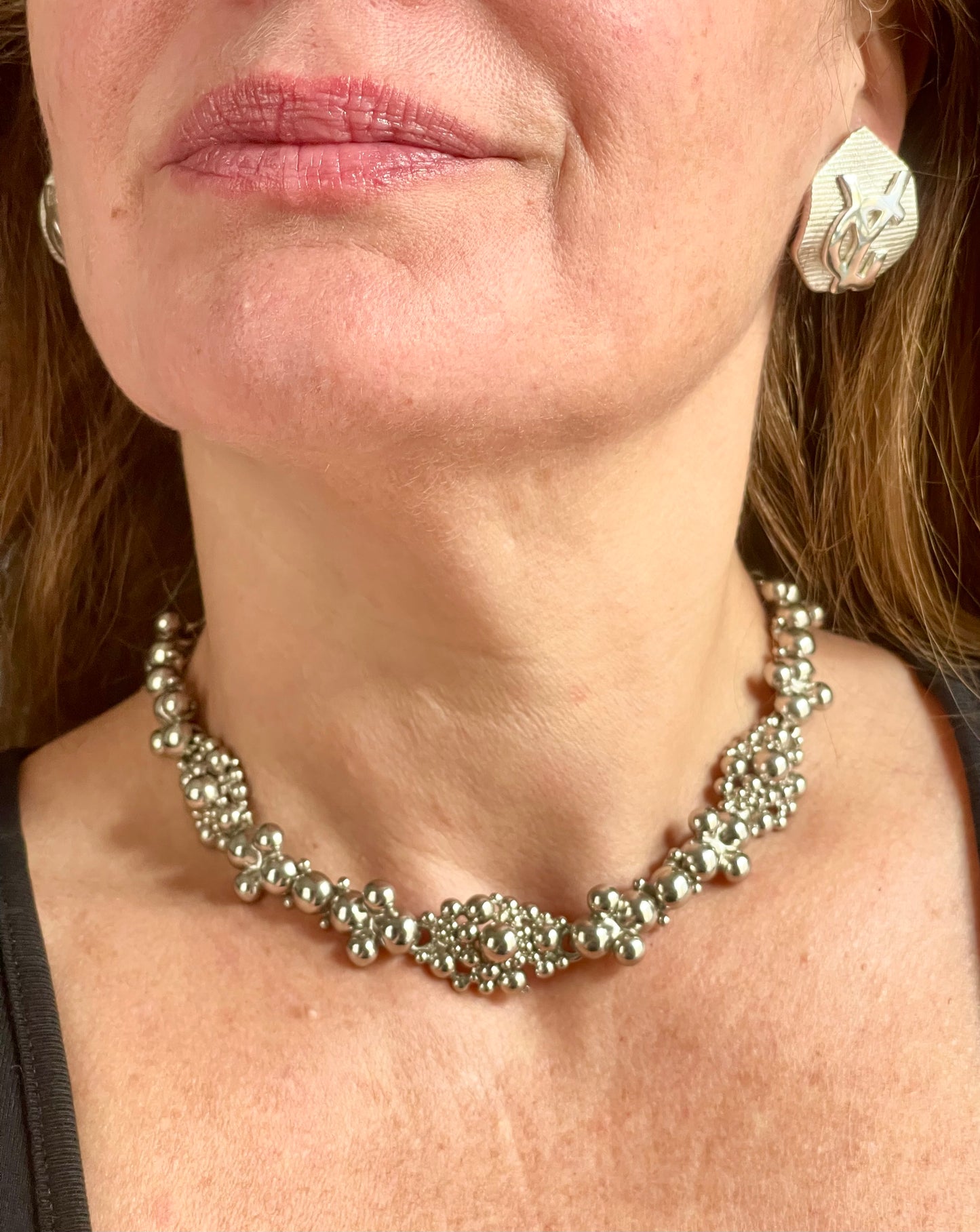 Side view of a model wearing a vintage Yves Saint Laurent silver necklace with hexagonal YSL Monogram earrings.