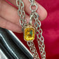 Silver chain necklace with a yellow gemstone of the Paco Rabanne silver mesh handmade bag held by a hand against a red background