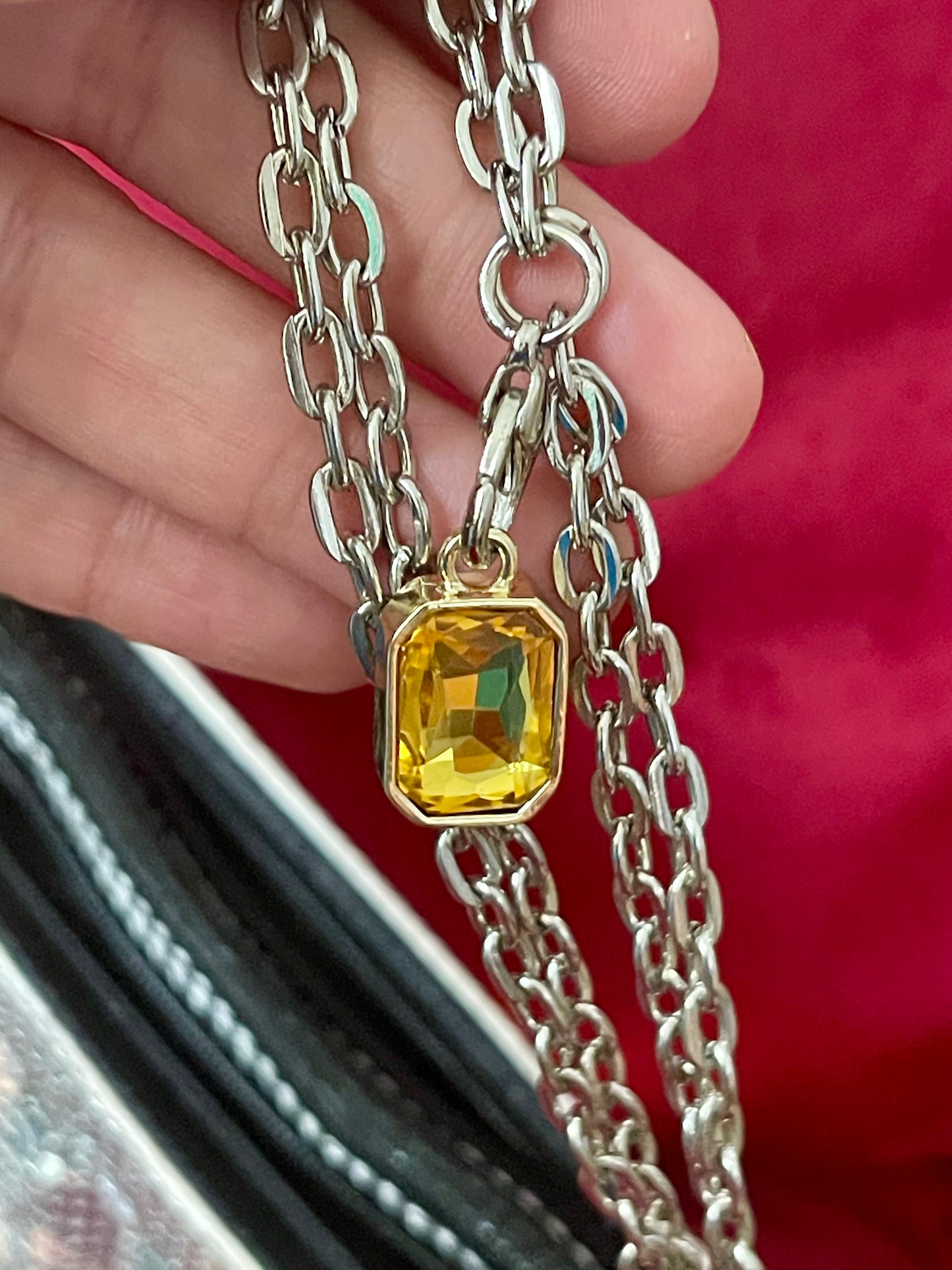 Silver chain necklace with a yellow gemstone of the Paco Rabanne silver mesh handmade bag held by a hand against a red background