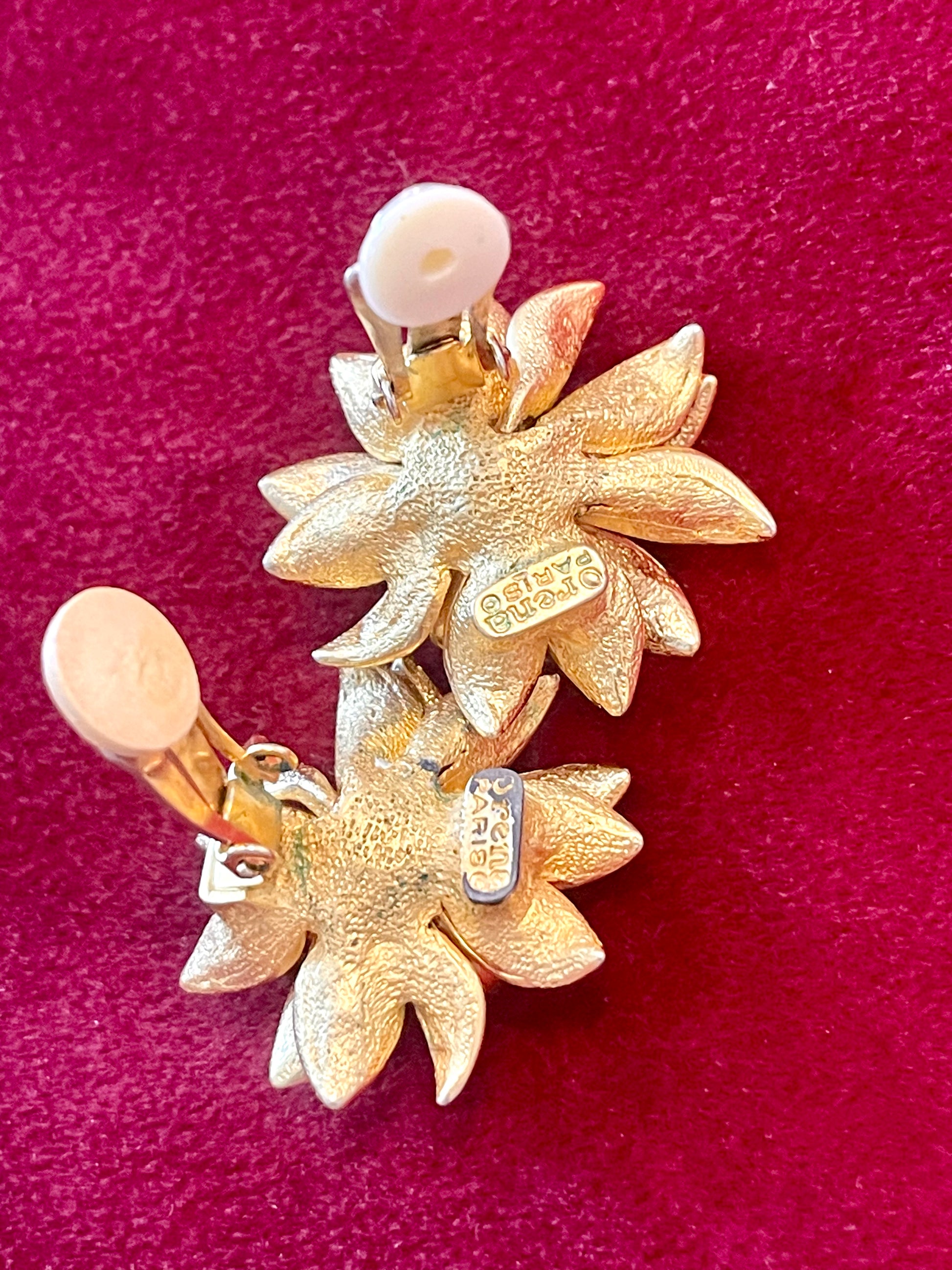 Close up in hallmark signature Orena Paris vintage gold sunflower-shaped earrings on a red background