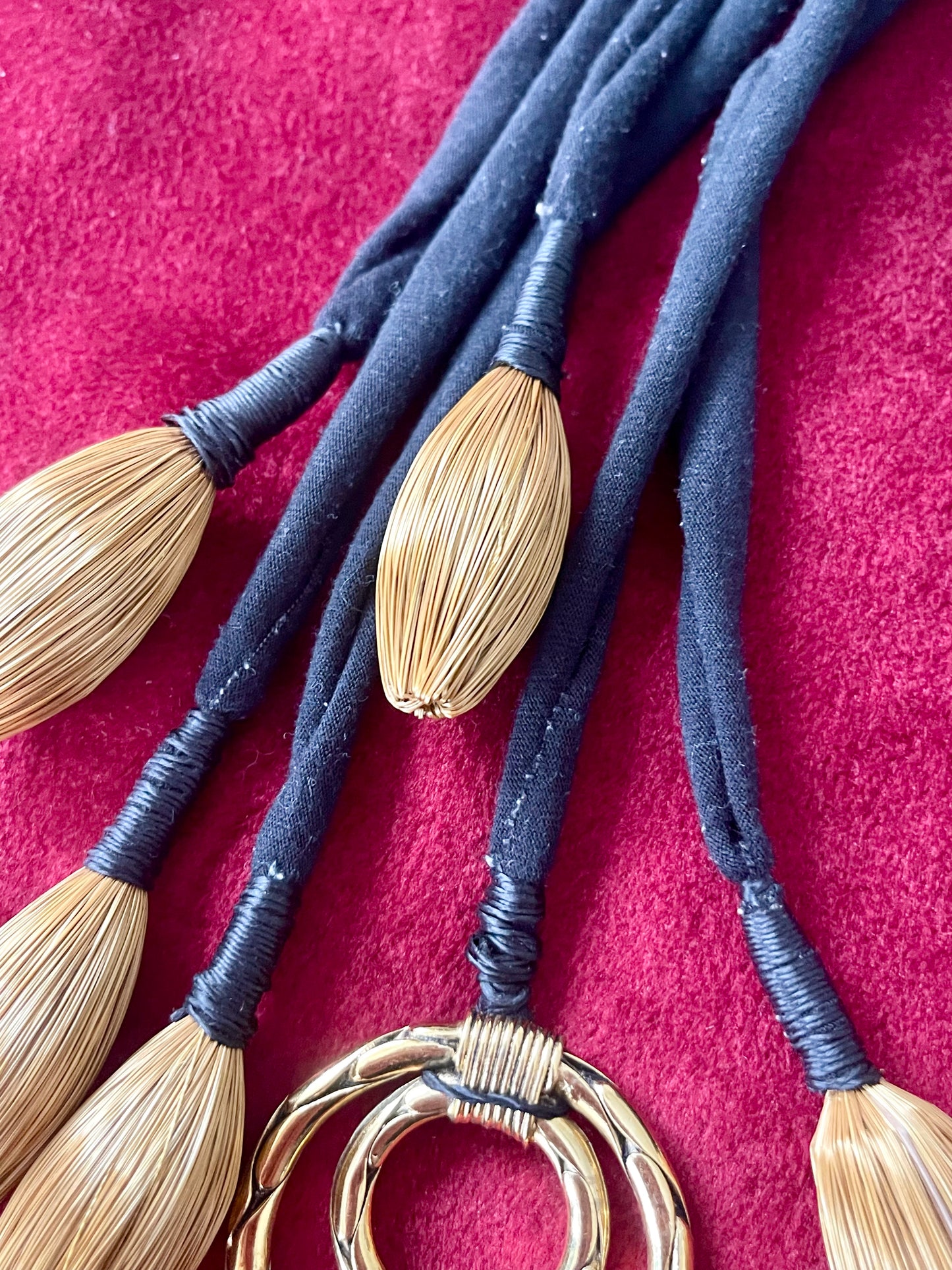 Close up of Art textile necklace with black fabric cords and gold tone pompom elements