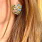 Close up of a person wearing   gold-tone vintage Yves Saint Laurent heart-shaped clip-on earrings decorated with multi-colored crystals vintage 80s