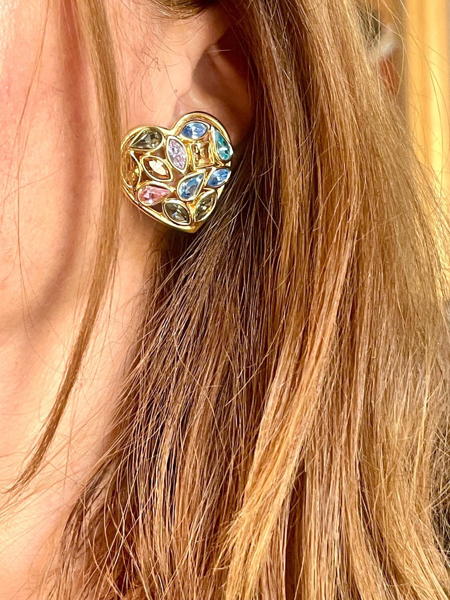 Close up of a person wearing   gold-tone vintage Yves Saint Laurent heart-shaped clip-on earrings decorated with multi-colored crystals vintage 80s