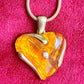 Close up on heart-shaped YSL pendant with gold and orange finish on a pink background