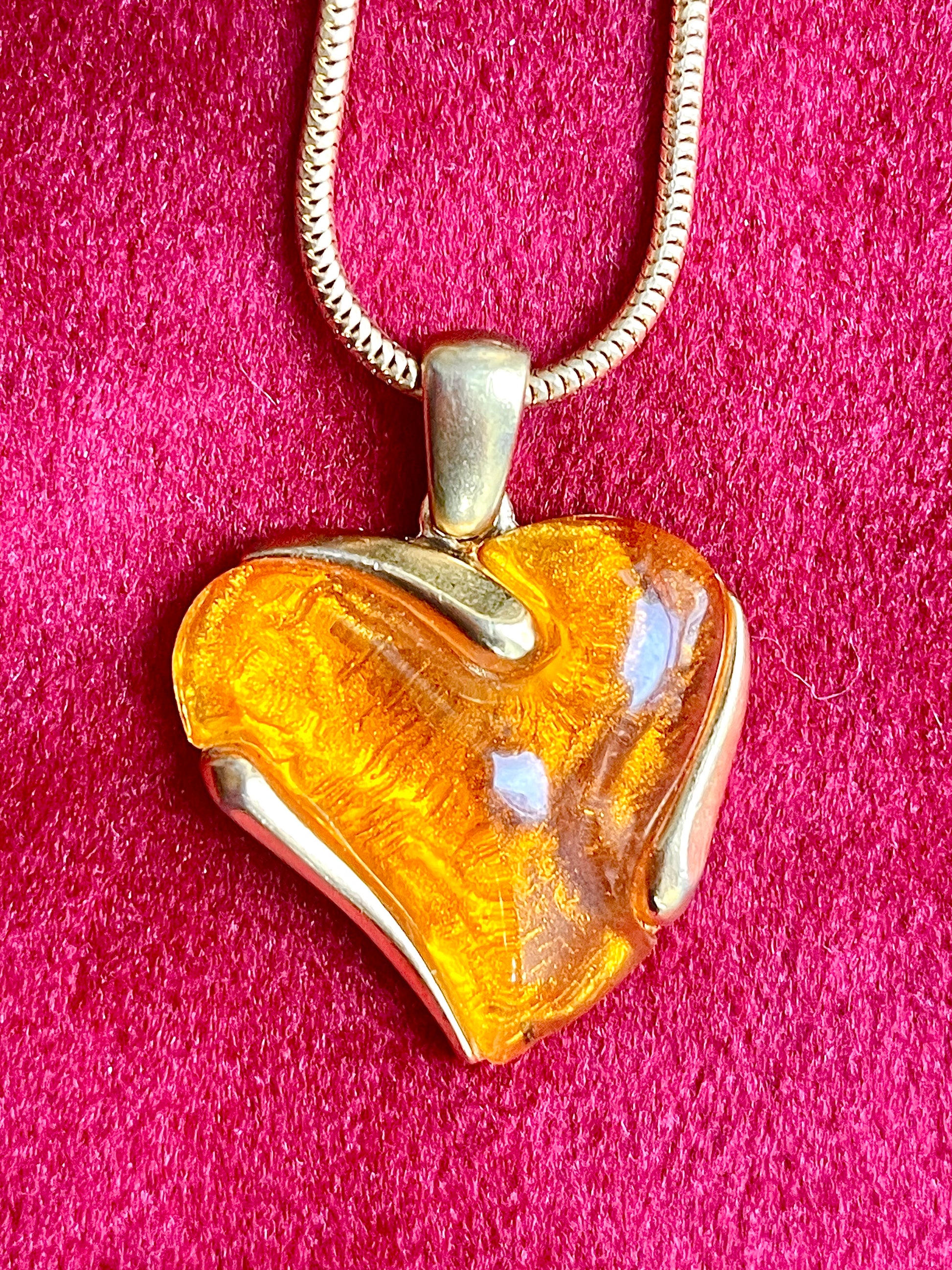 Close up on heart-shaped YSL pendant with gold and orange finish on a pink background