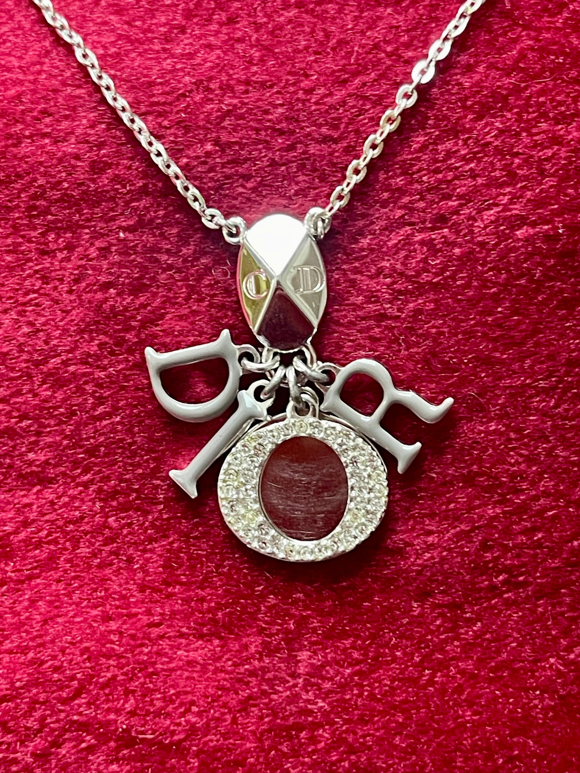 Close-up view of a short silver-tone Dior necklace with grey enameled letter charms on a red velvet background.