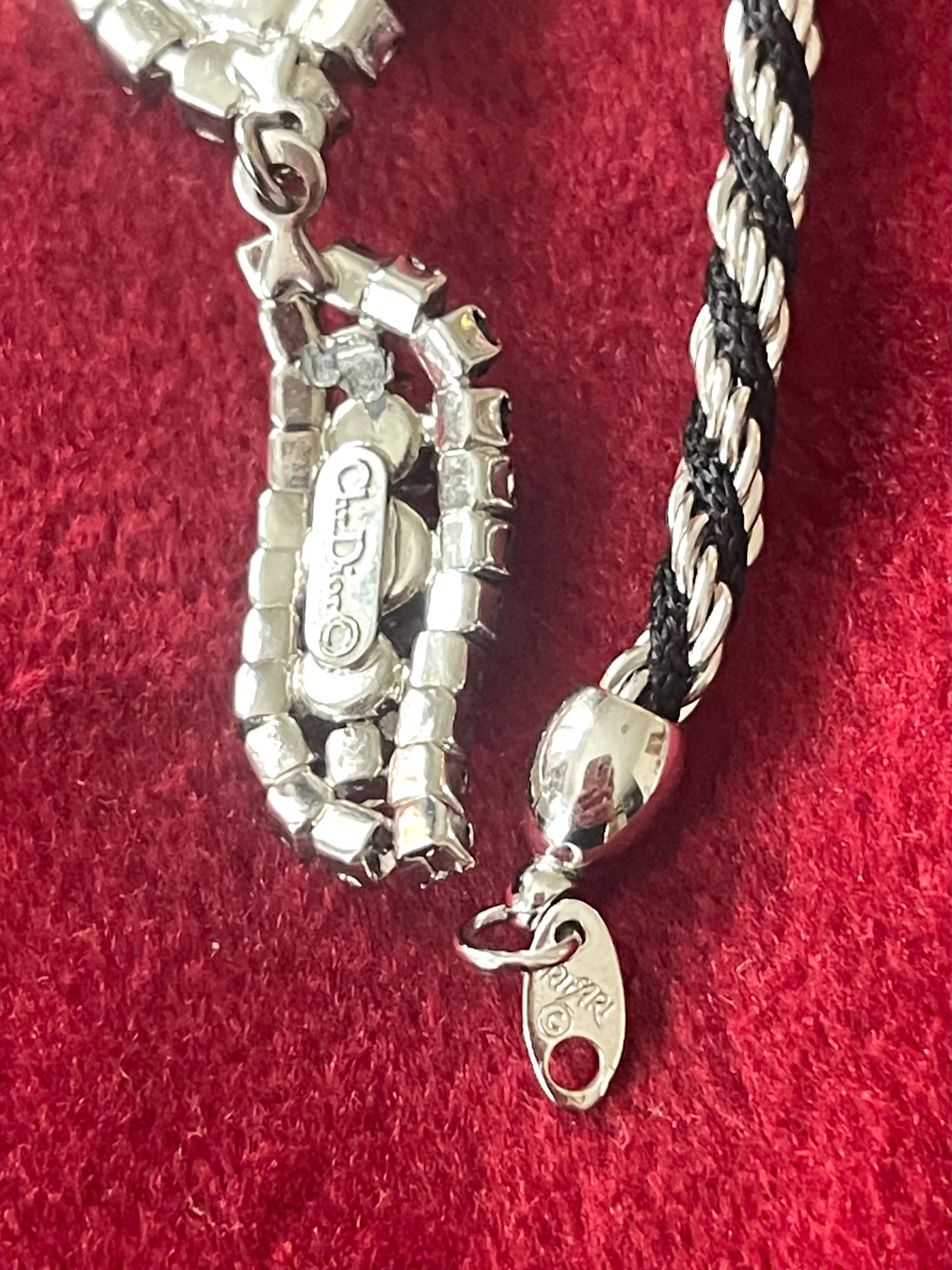 Close up on signature of Vintage Trifari silver-tone rope necklace,  Christian Dior crystal pendant, photographed on a red background.