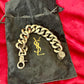Chunky Yves Saint Laurent bronze and grey chain flat over black clothing, highlighting its unisex modern design