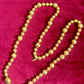Vintage Yves Saint Laurent gold beaded necklace with textured graduated beads displayed on red velvet background.
