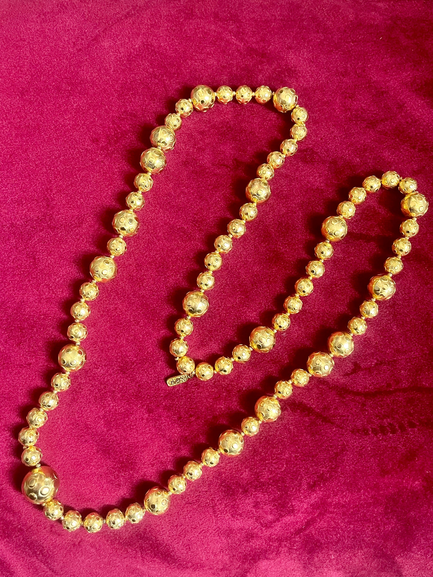 Vintage Yves Saint Laurent gold beaded necklace with textured graduated beads displayed on red velvet background.