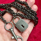 Display on hand close up on Vintage Saint Laurent upcycled necklace featuring a dark gunmetal chain with original lock and key charm pendant, repurposed from a Saint Laurent keychain