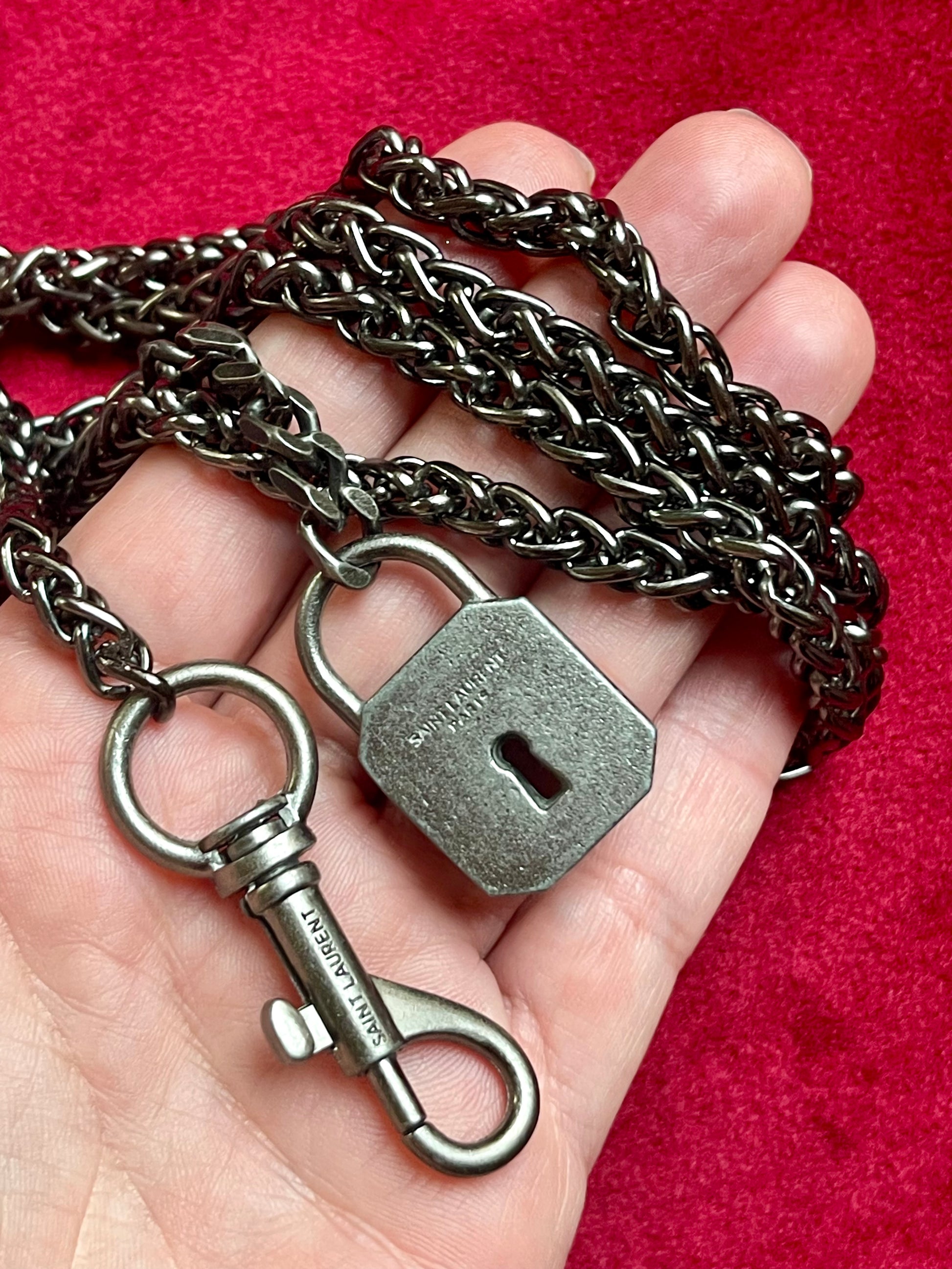 Display on hand close up on Vintage Saint Laurent upcycled necklace featuring a dark gunmetal chain with original lock and key charm pendant, repurposed from a Saint Laurent keychain