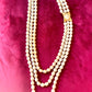 Vintage Yves Saint Laurent faux pearl multi-strand necklace with gold-tone clasp displayed on a red velvet background.