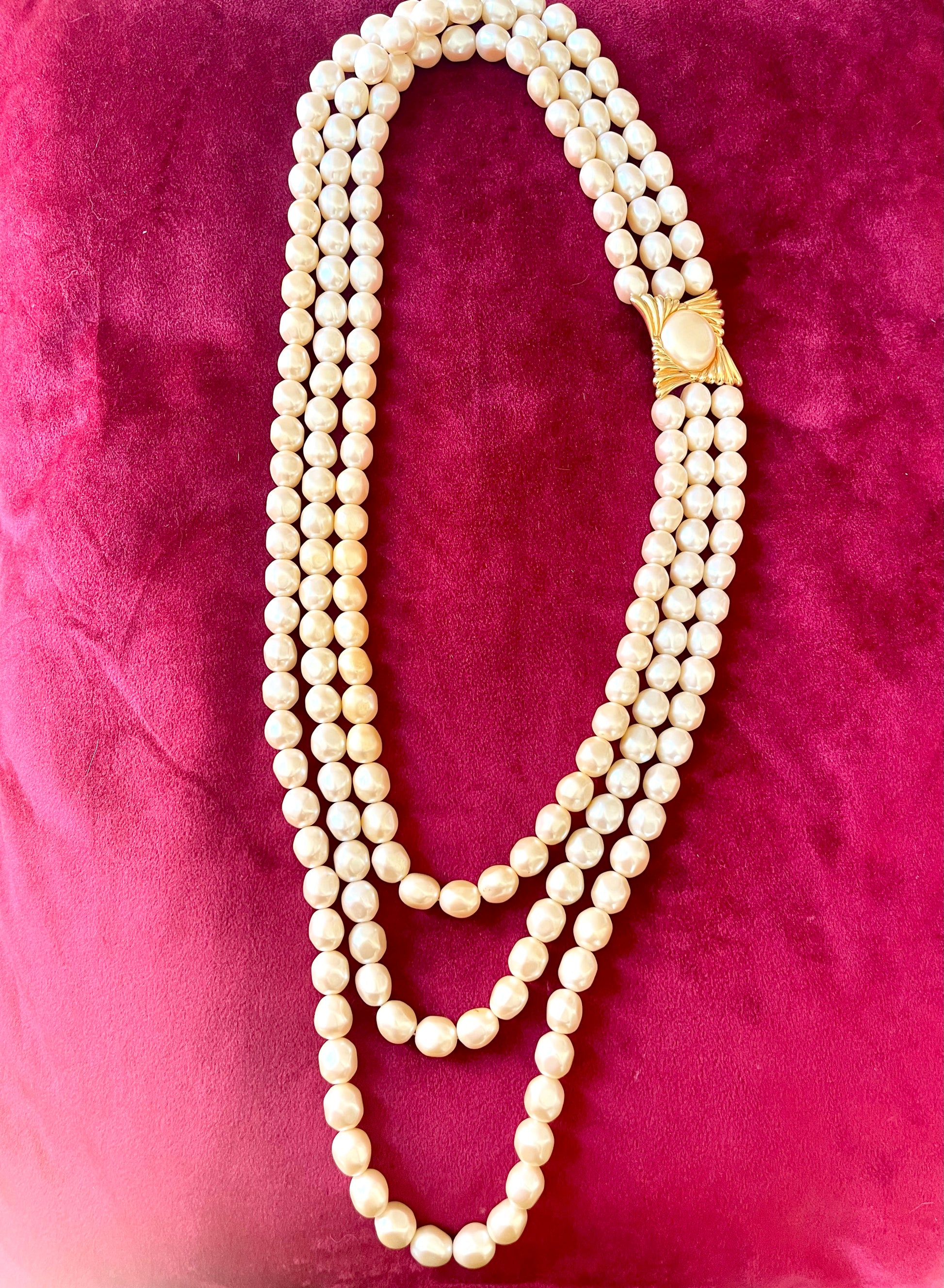 Vintage Yves Saint Laurent faux pearl multi-strand necklace with gold-tone clasp displayed on a red velvet background.