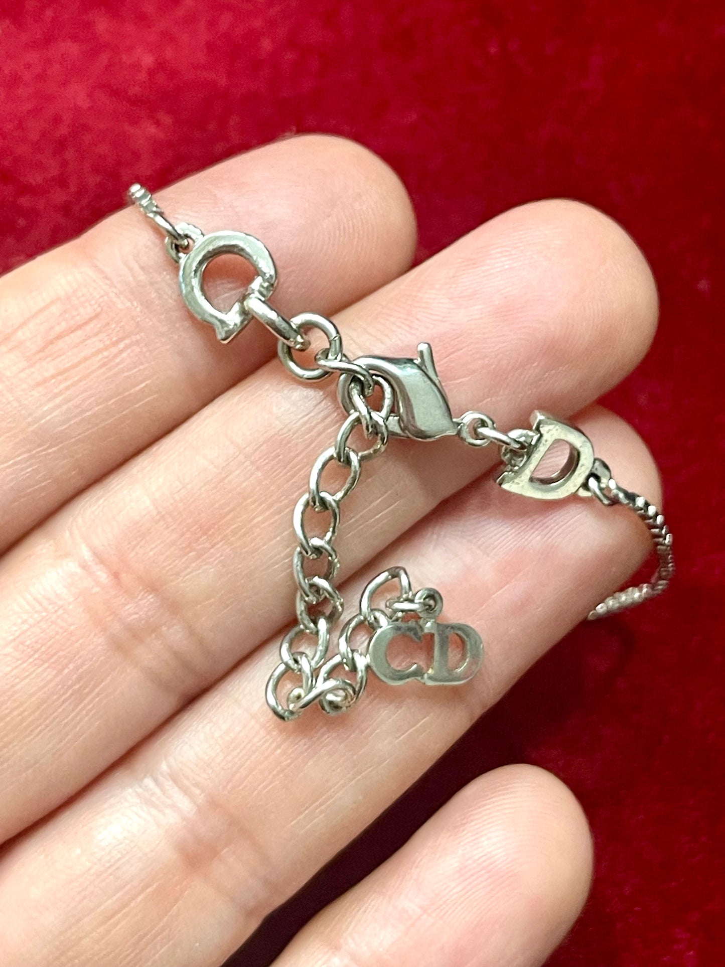 Silver Dior bracelet with charms on a hand against a red background heart shaped lock vintage Christian Dior 
