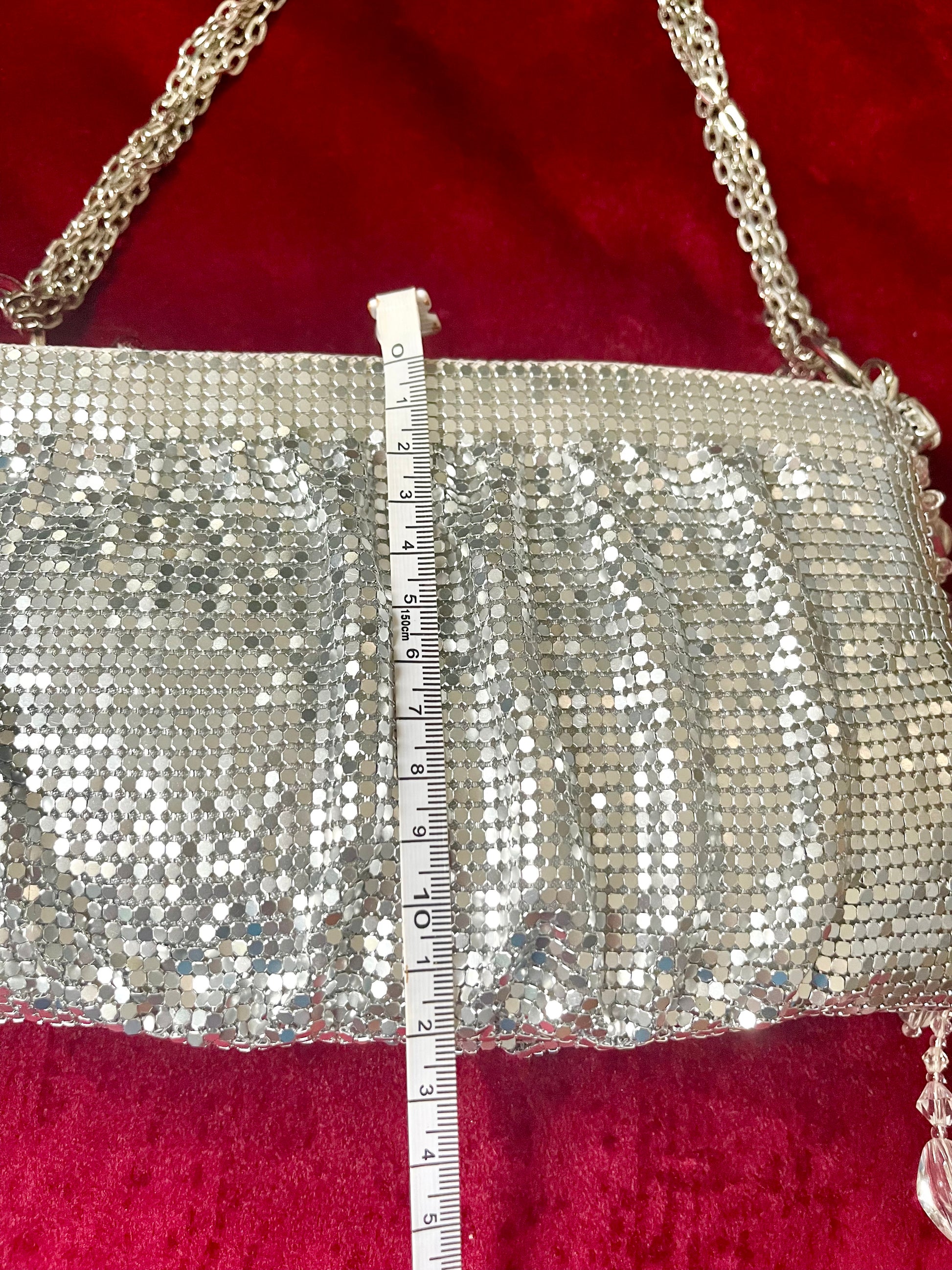 Length measurement of the One of a kind handmade Paco Rabanne repurposed silver pixel mesh bag using a measuring tape on a red background 