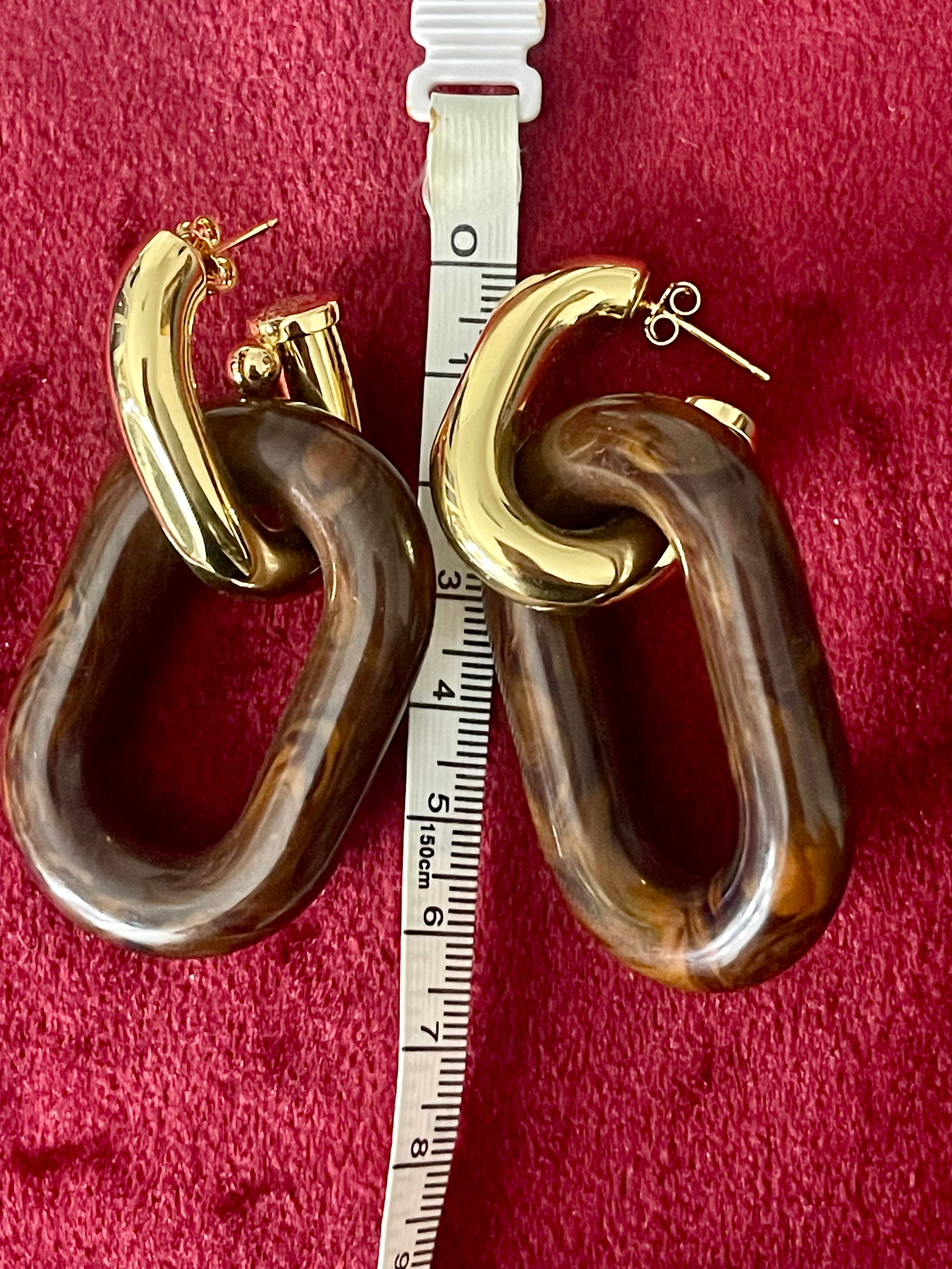 Gold and brown Paco Rabanne hoop XL link earrings on a red background with a ruler for scale.