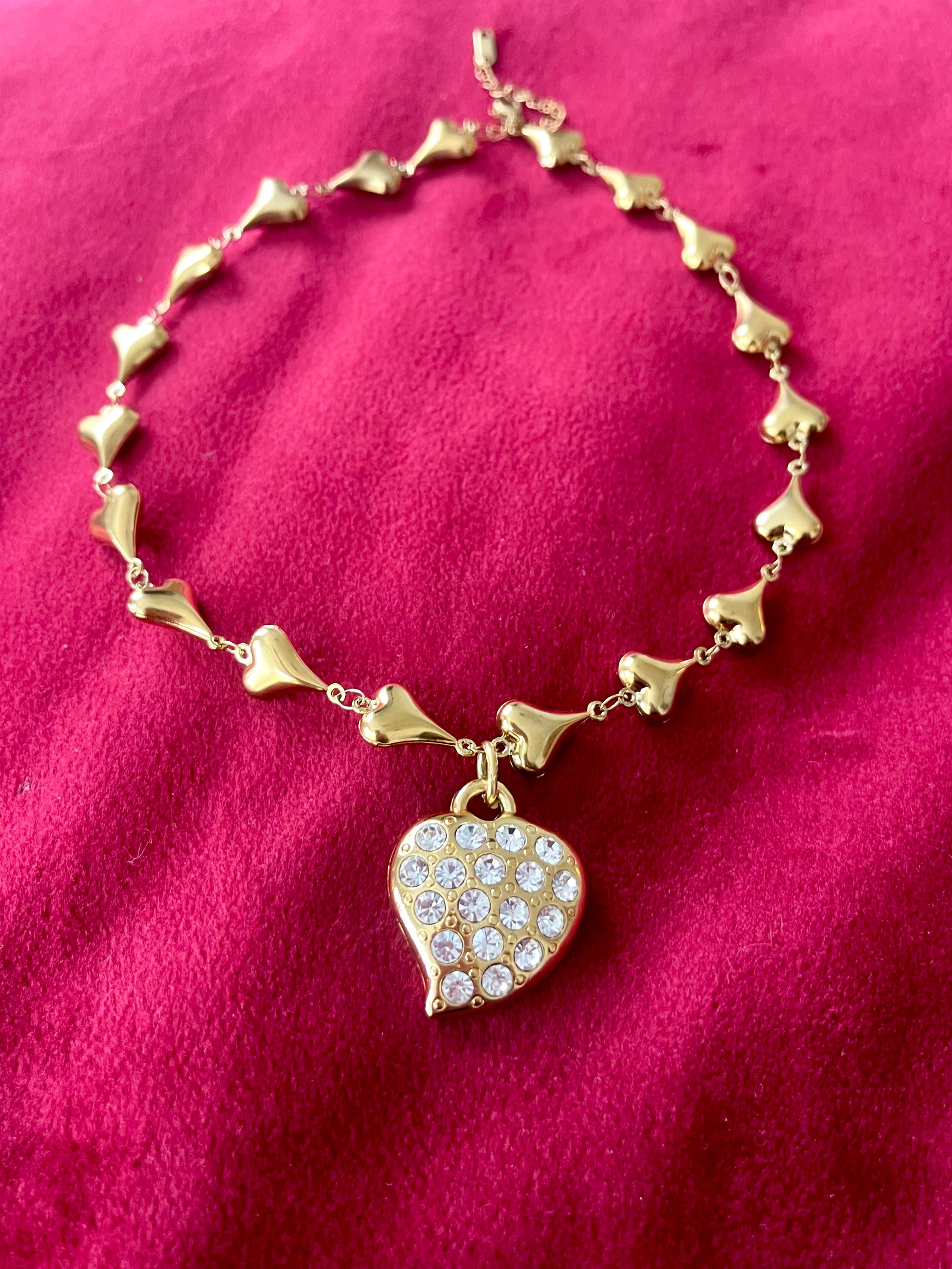 Vintage Yves Saint Laurent heart rhinestone pendant necklace with gold stainless steel chain on pink background