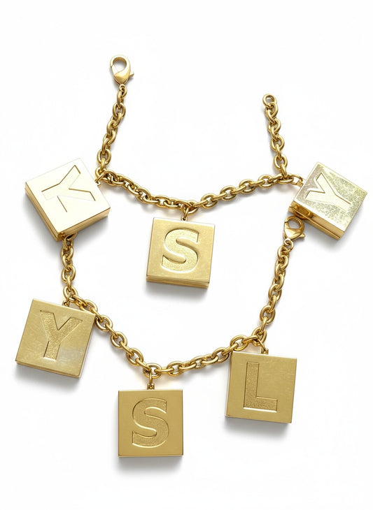 Gold Yves Saint Laurent Perfumes bracelet with square charms featuring letters on a white background