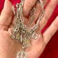 Hand holding multiple upcycled Dior silver chains with charms against a red background