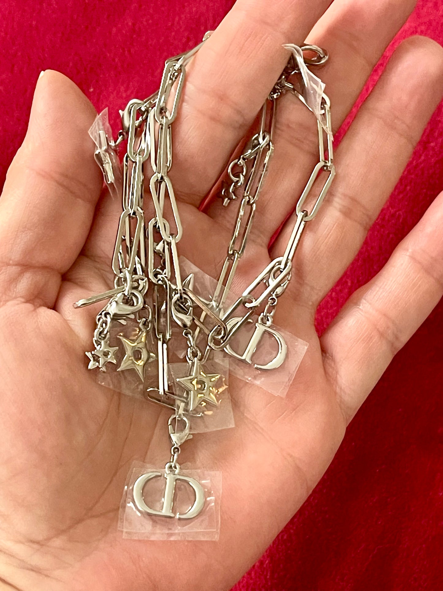 Hand holding multiple upcycled Dior silver chains with charms against a red background