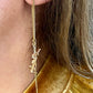Gold earring with a small YSL pendant worn by a person with blonde hair.