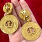 Back of Yves Saint Laurent gold-tone anchor earrings with engraved signatures red background Displayed on hand