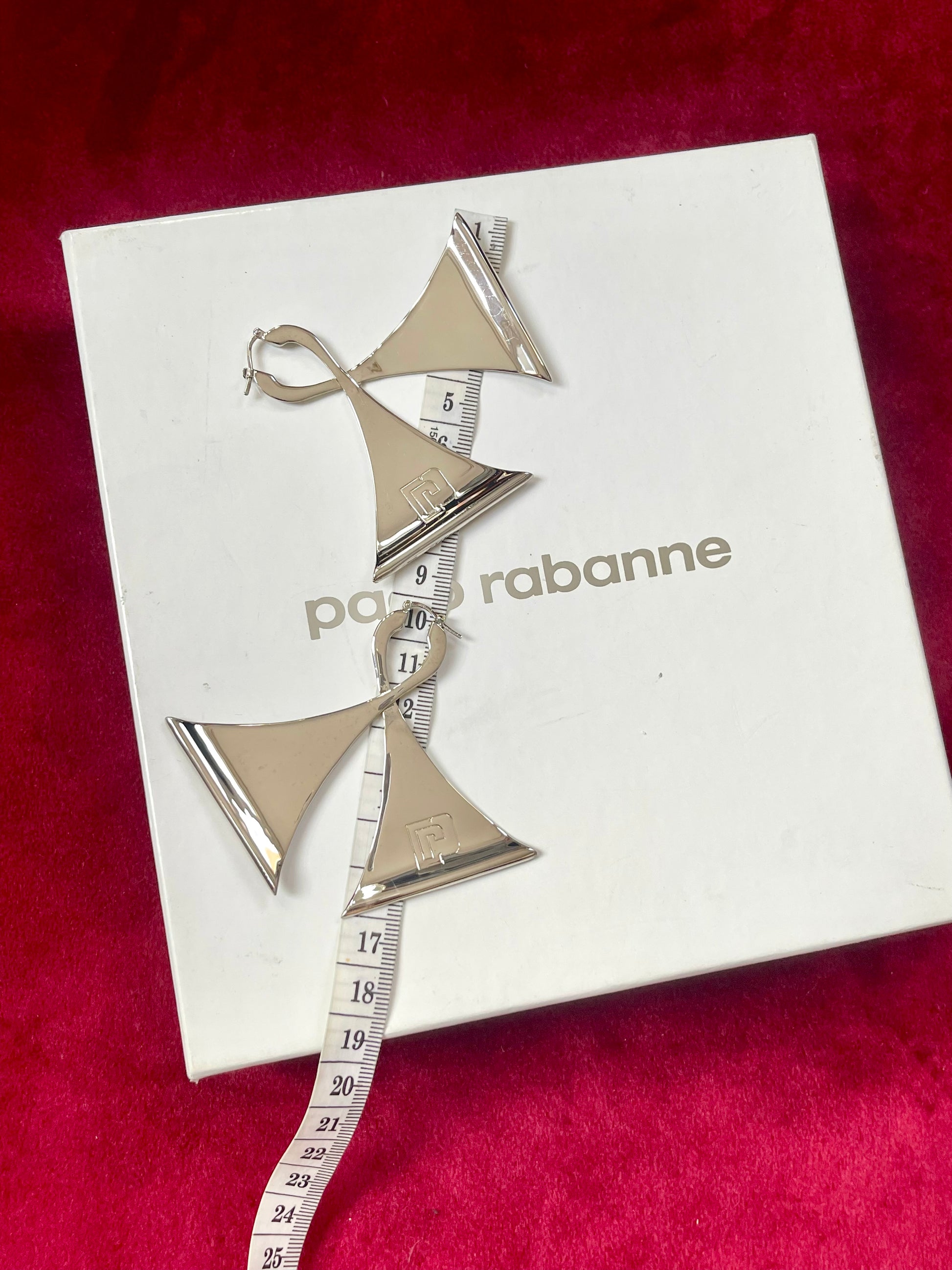 Showing measurements of Vintage Paco Rabanne silver-tone geometric sculptural statement earrings using a measuring tape on red background 