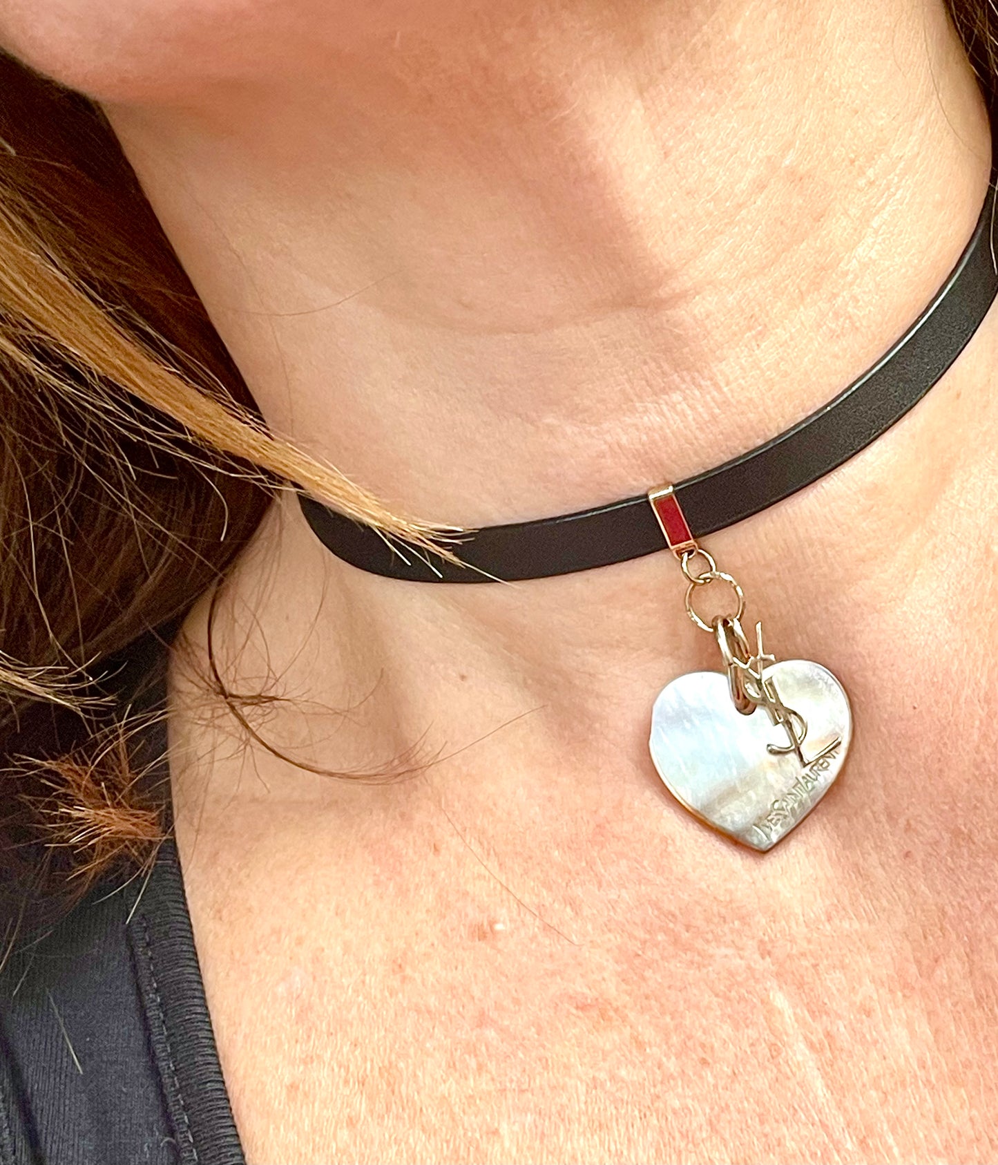 Close up of a Person wearing a black leather Yves Saint Laurent choker necklace with a heart-shaped pendant and logo charm YSL