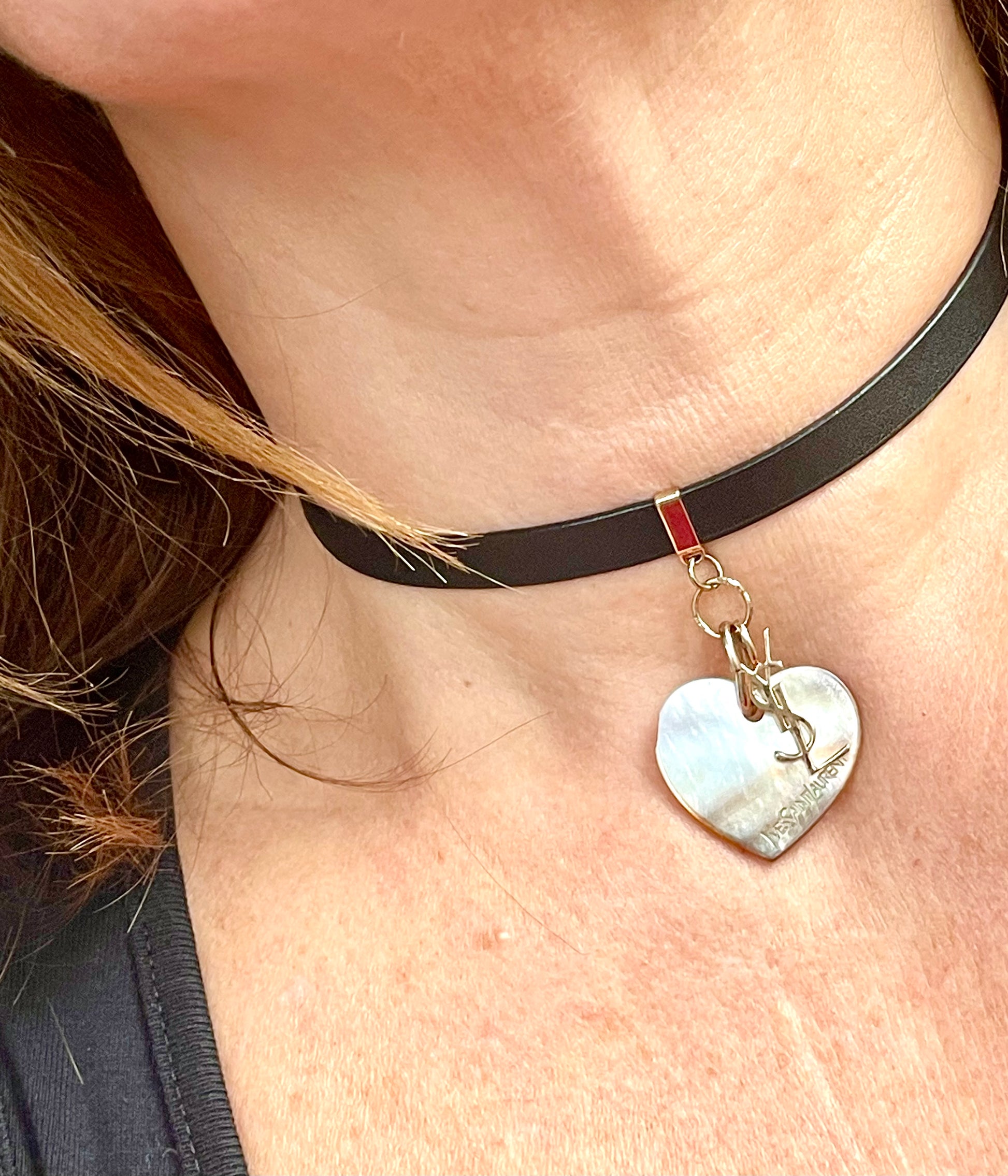 Close up of a Person wearing a black leather Yves Saint Laurent choker necklace with a heart-shaped pendant and logo charm YSL