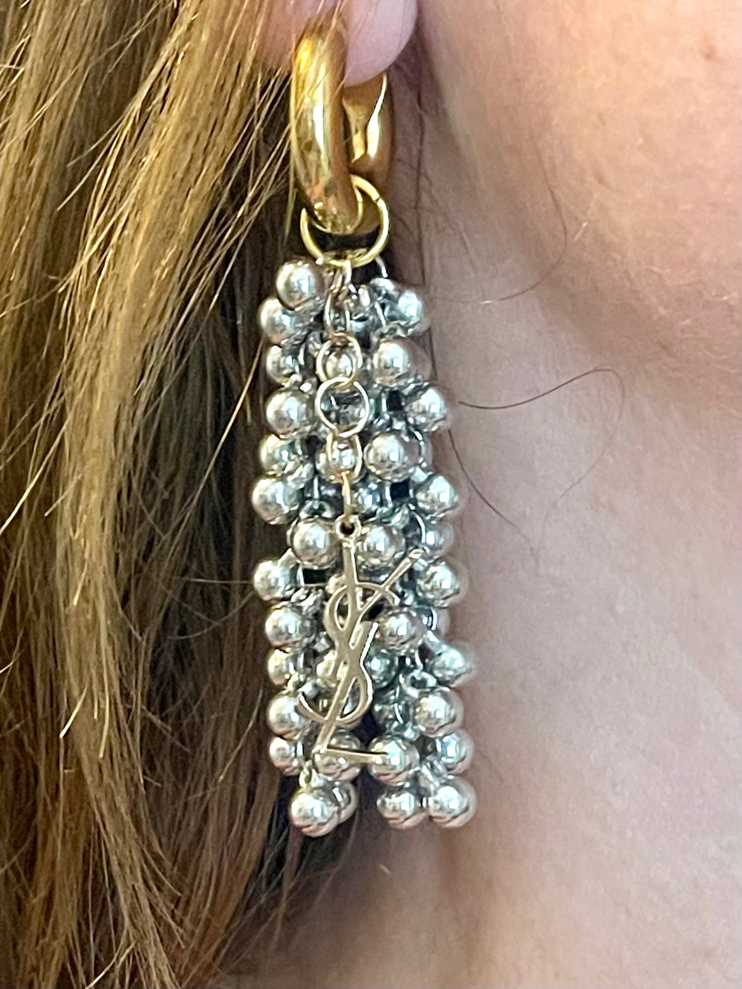 Close up of Gold and silver earrings with pearl-like beads and YSL Yves Saint Laurent charms worn by model