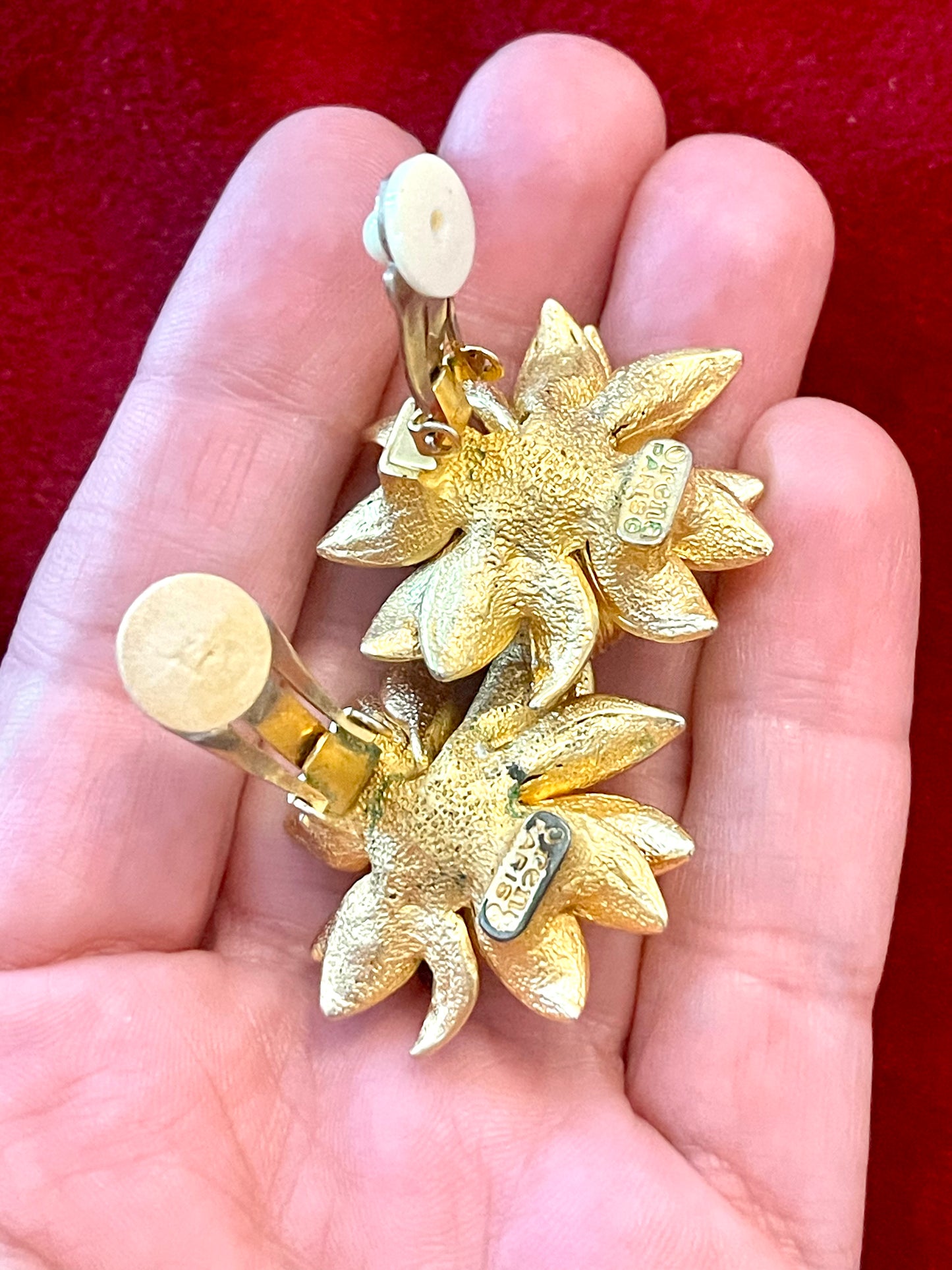 Back side view Orena Paris vintage gold sunflower-shaped earrings placed on hand palm on a red background