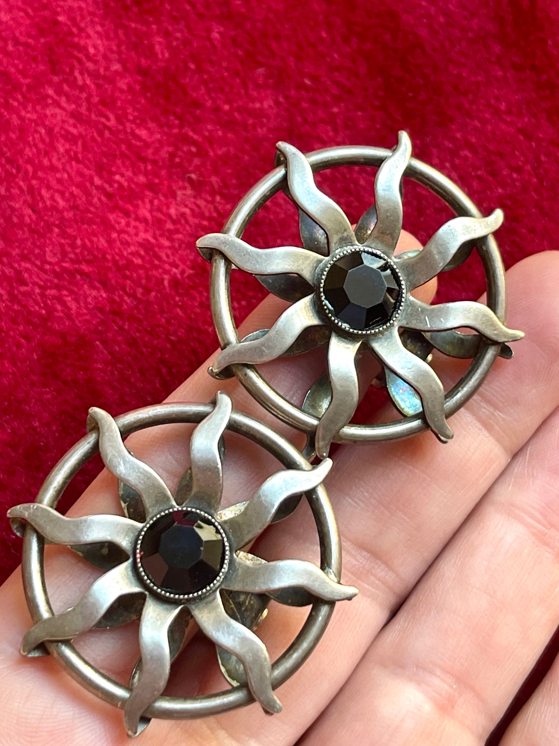 Hand holding a pair of 1980s Paco Rabanne silver-tone sun earrings with dark faceted center stones, highlighting detailing and condition.